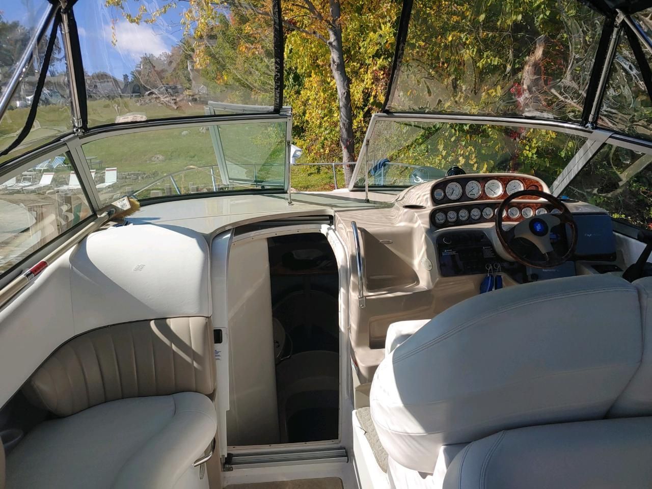 The cockpit of a boat with white seats and a wooden steering wheel.