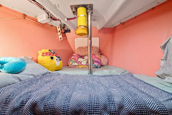 Cozy cabin bed in a 1989 Concordia 52 sailboat with colorful pillows and pink walls.