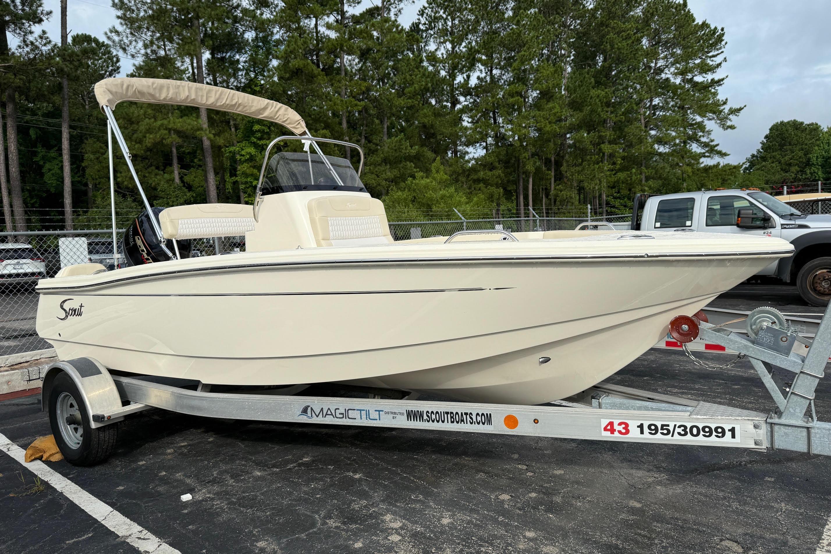 2026 Scout 188 Sportfish boat on trailer, parked in a lot with trees in background.