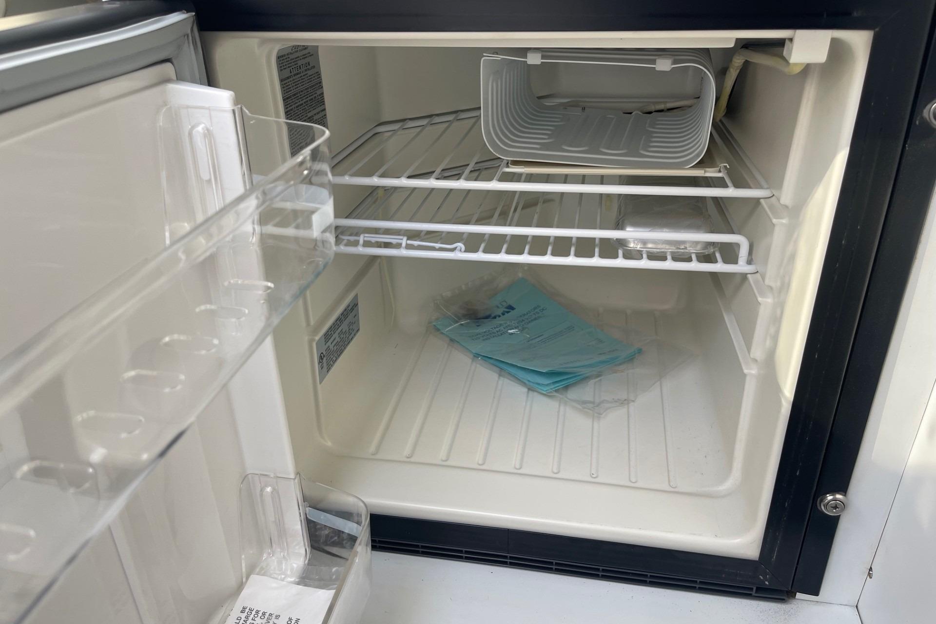 Empty refrigerator interior with shelves, documents, and a small container inside a 2004 Formula 382 FASTech.