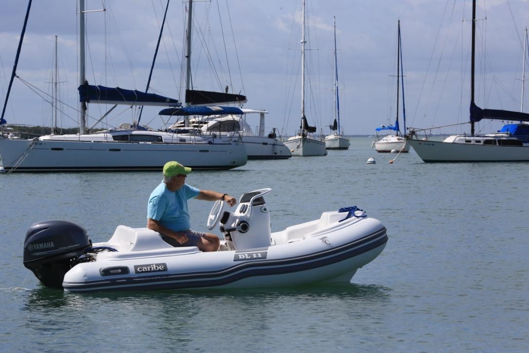 Man operating 2025 Caribe DL11 inflatable boat in marina with sailboats.