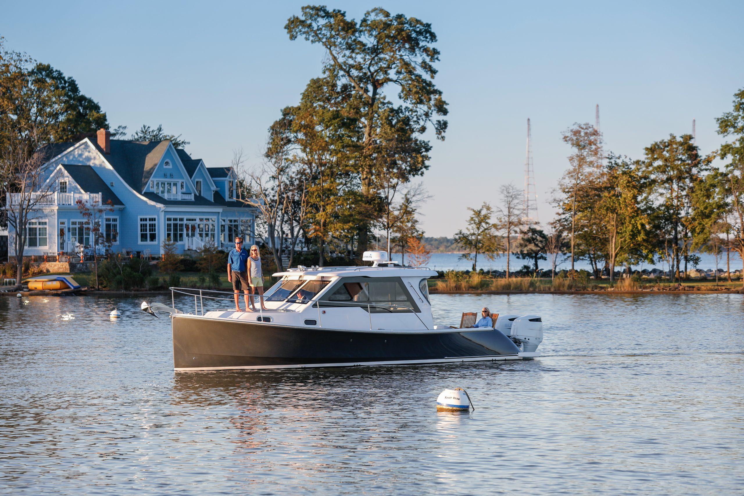 2024 True North 34 boat cruising near a lakeside house with trees in the background.