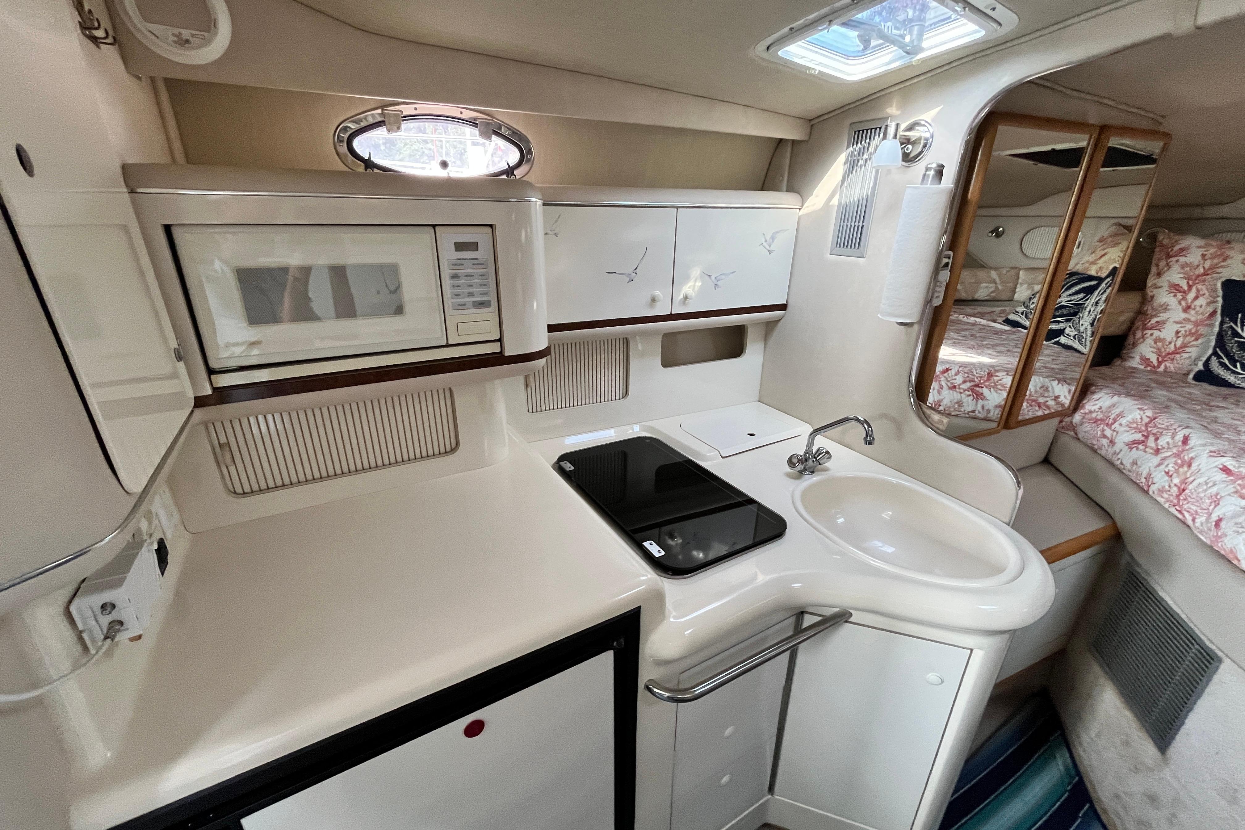 1995 Sea Ray Sundancer 330 interior with kitchenette, featuring microwave, sink, and cozy sleeping area.