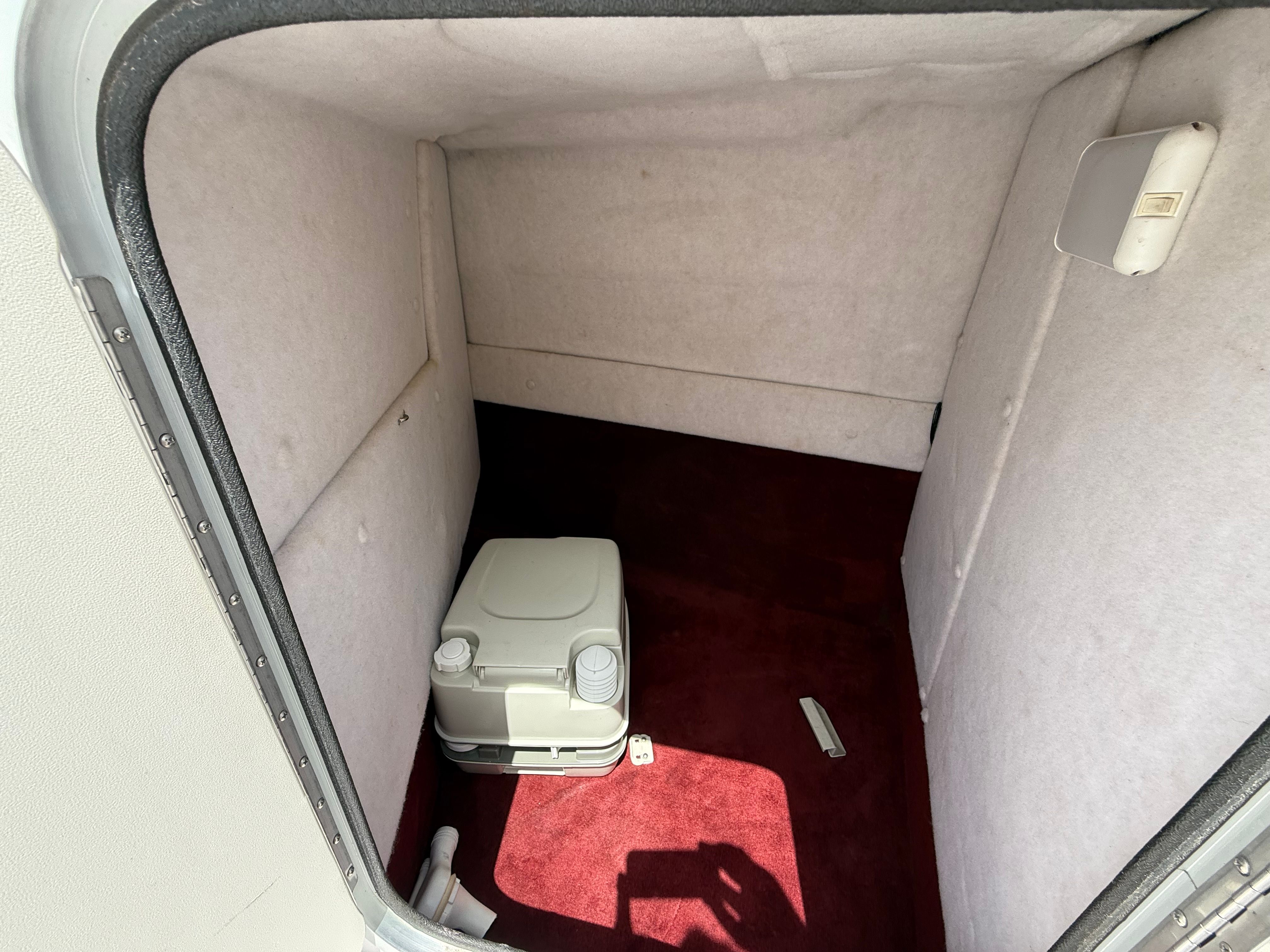 Interior of a boat with red carpet and a portable toilet.