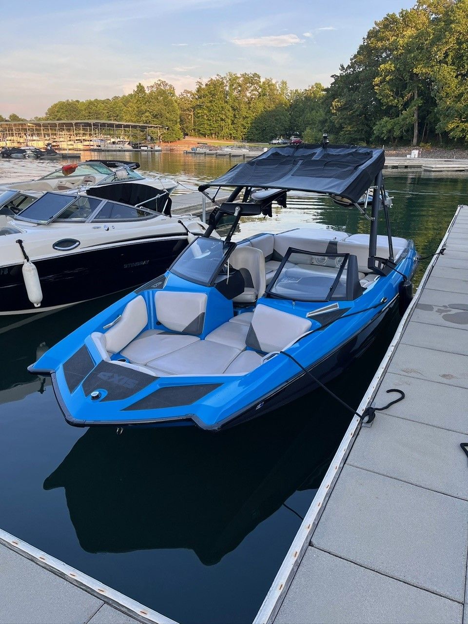 2014 Axis A22 boat docked, blue and white design, calm water, surrounded by trees.