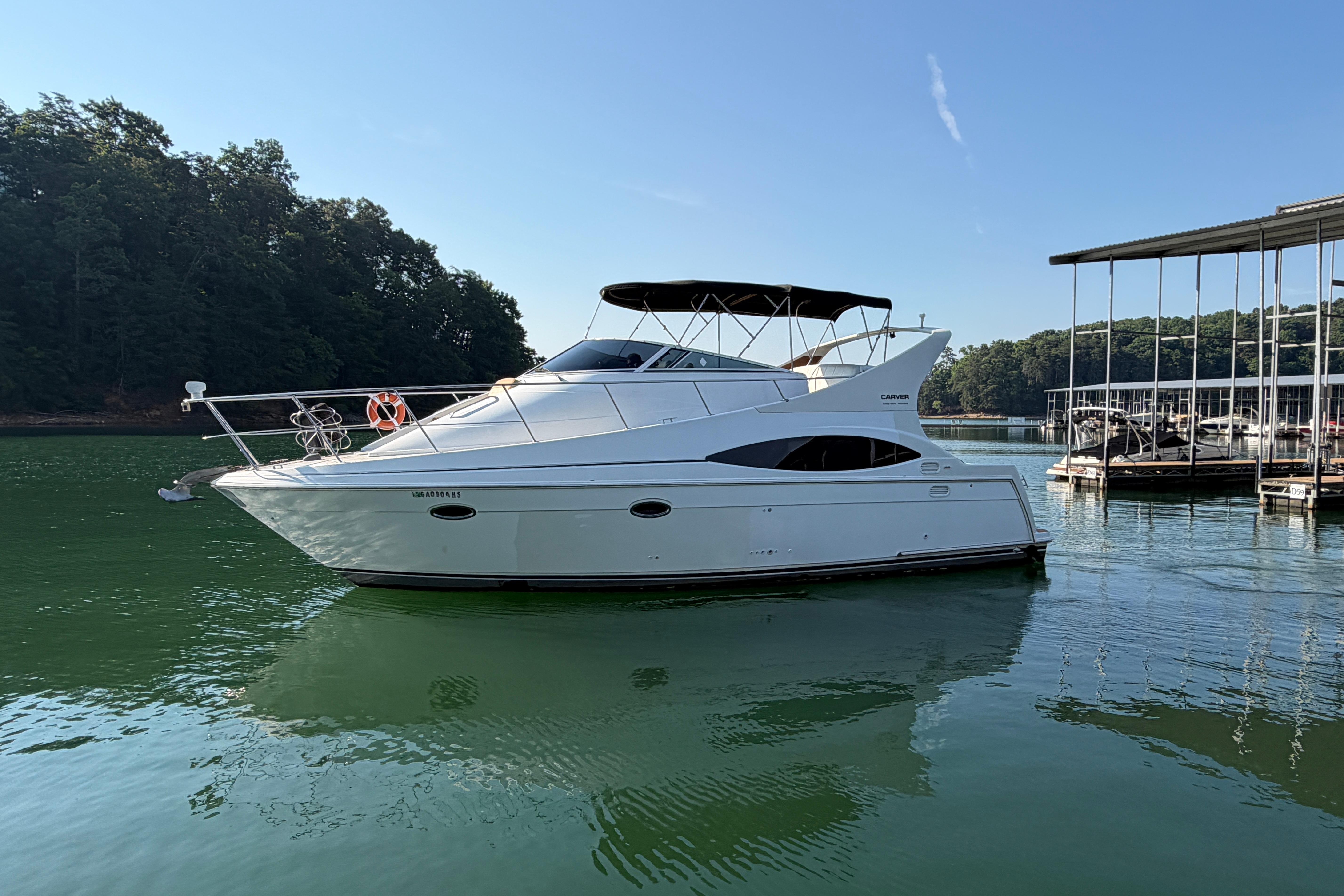 2003 Carver 350 Mariner yacht docked on serene lake with lush forest backdrop.