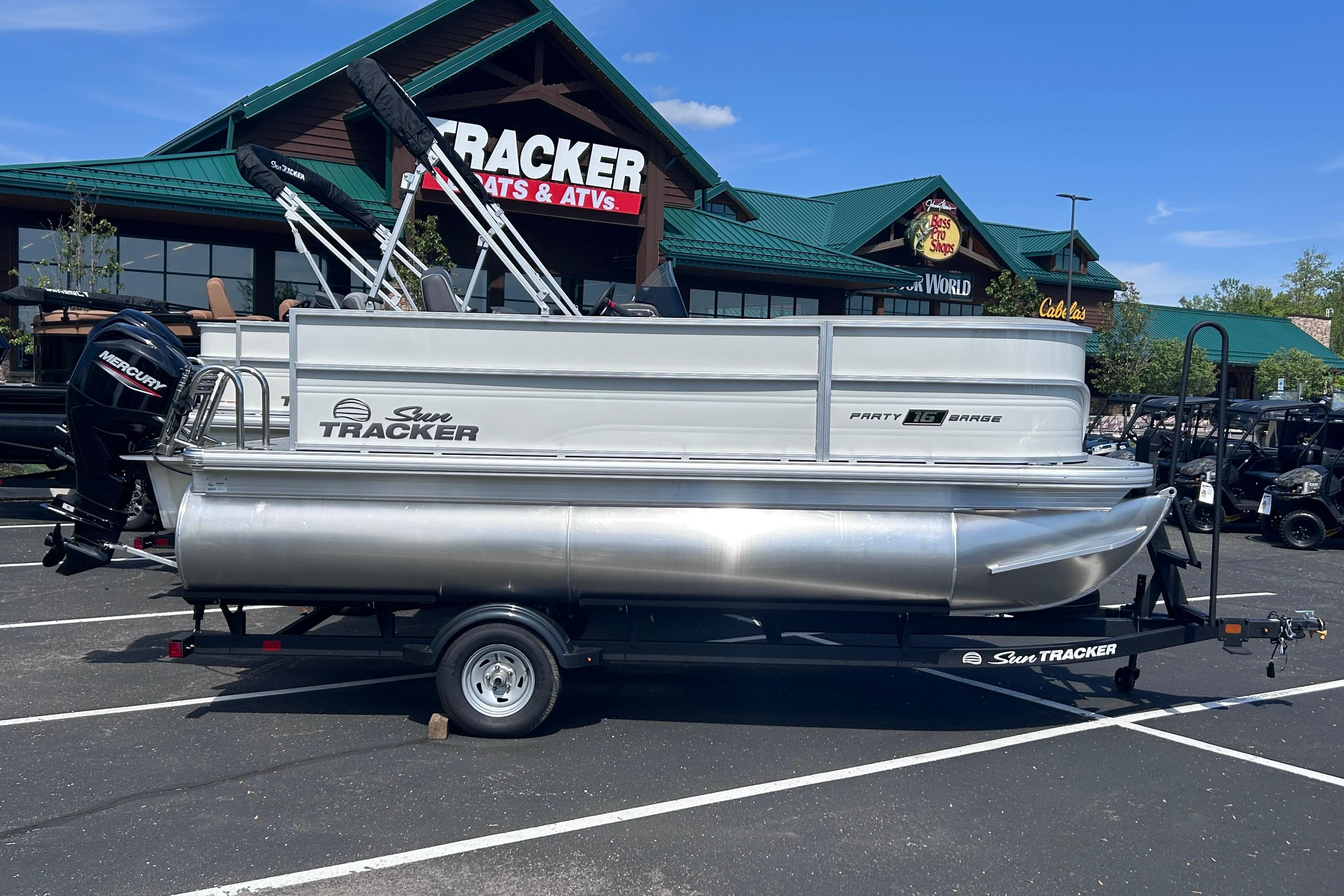 2026 Sun Tracker Party Barge 16 DLX pontoon boat on trailer, parked outside dealership.