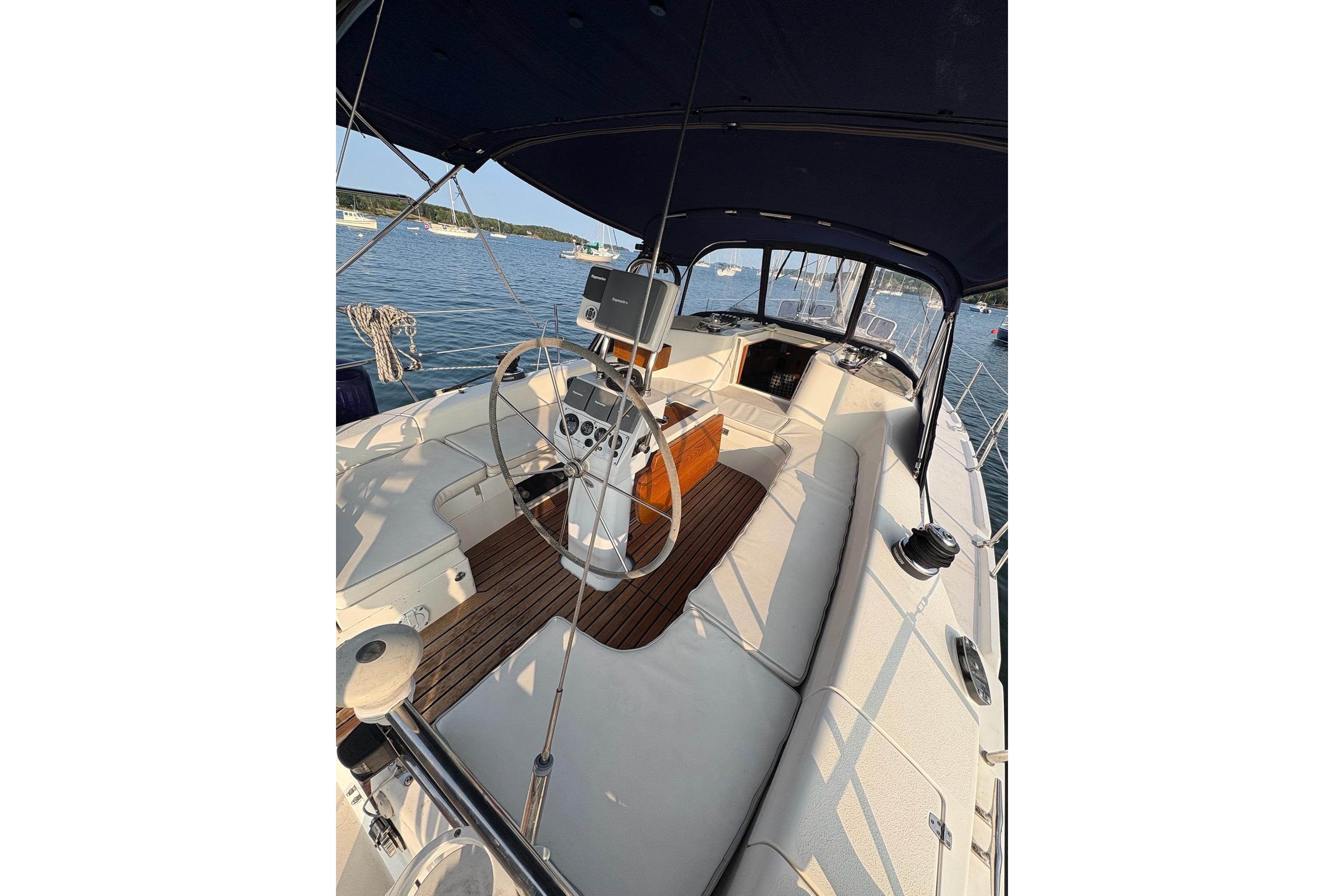 2003 Catalina 387 sailboat cockpit with steering wheel, wood accents, and canopy on calm water.