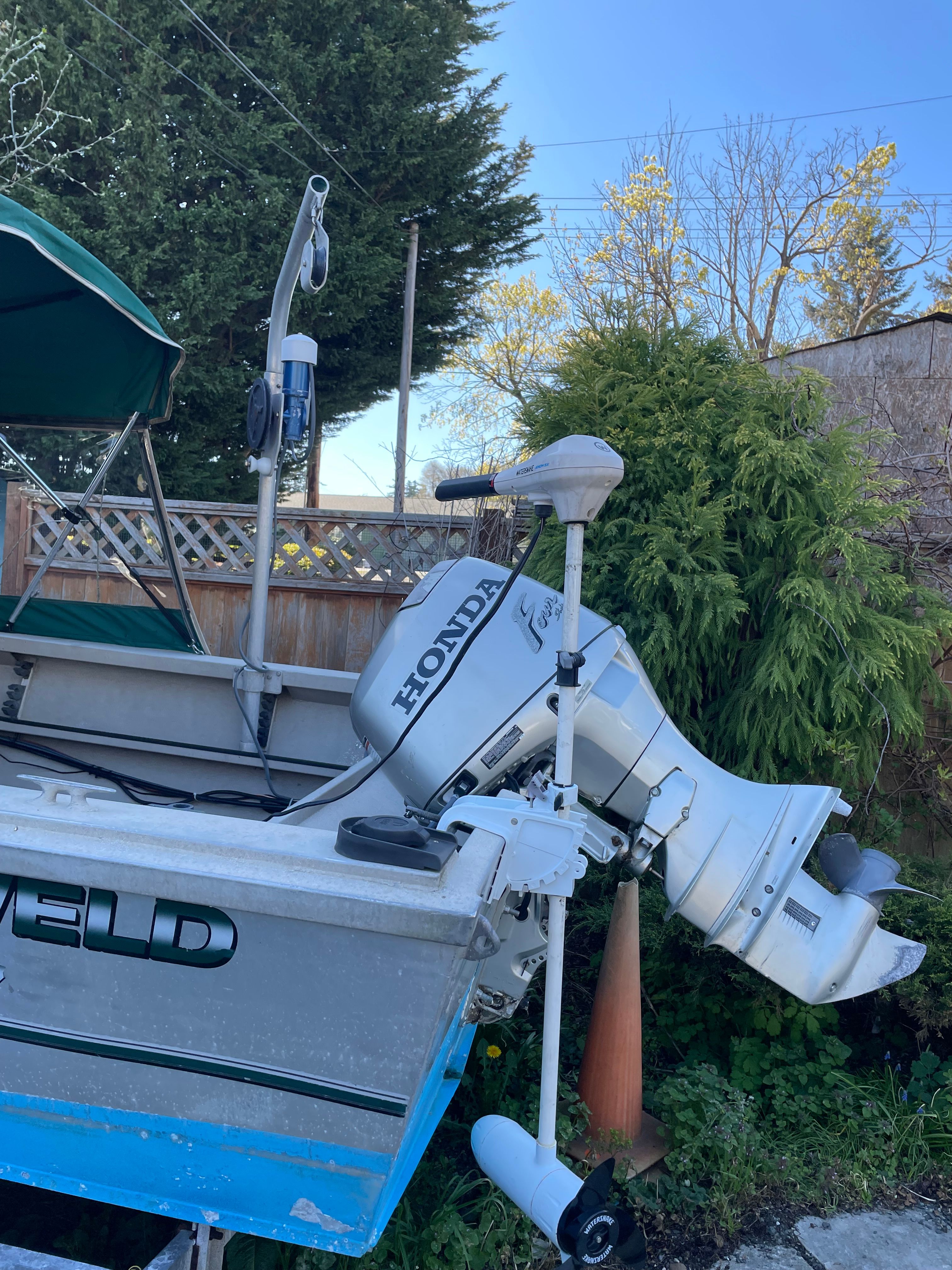 A 2001 Alumaweld Stryker boat with a Honda outboard motor, parked beside a wooden fence.