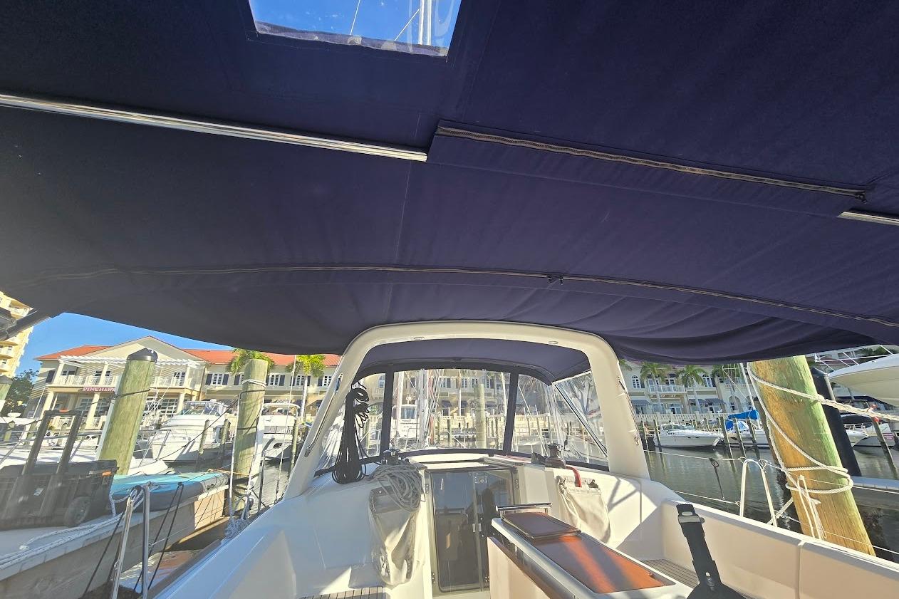 2023 Beneteau Oceanis 38.1 cockpit view with marina backdrop, featuring blue canopy.