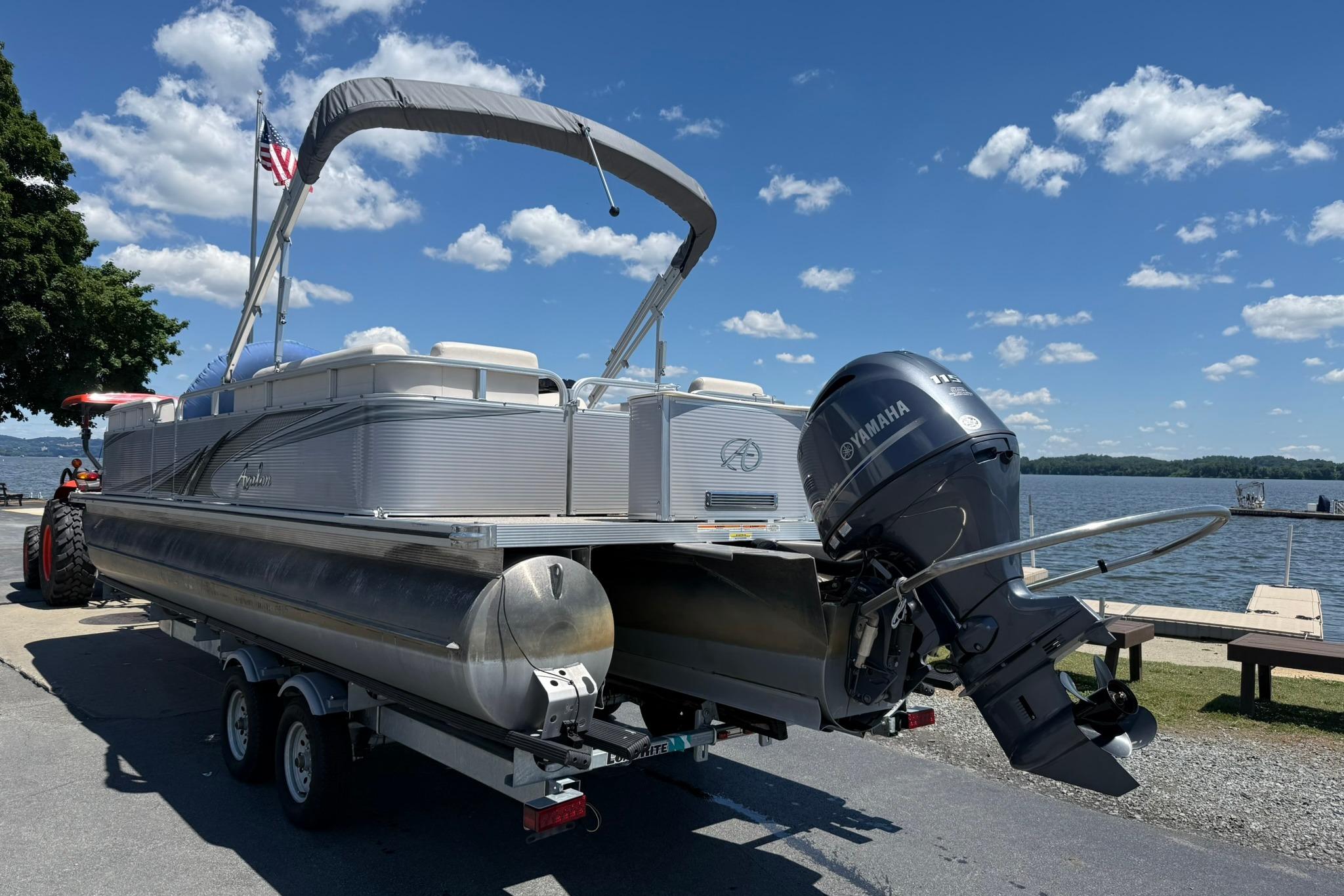2019 Avalon GS Quad Lounge 25' pontoon boat on trailer by a lake, sunny day.
