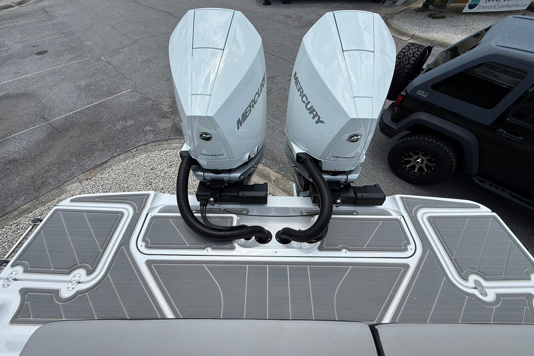 Twin Mercury outboard engines on a 2027 Monterey Elite 30 OB boat, parked near a vehicle.