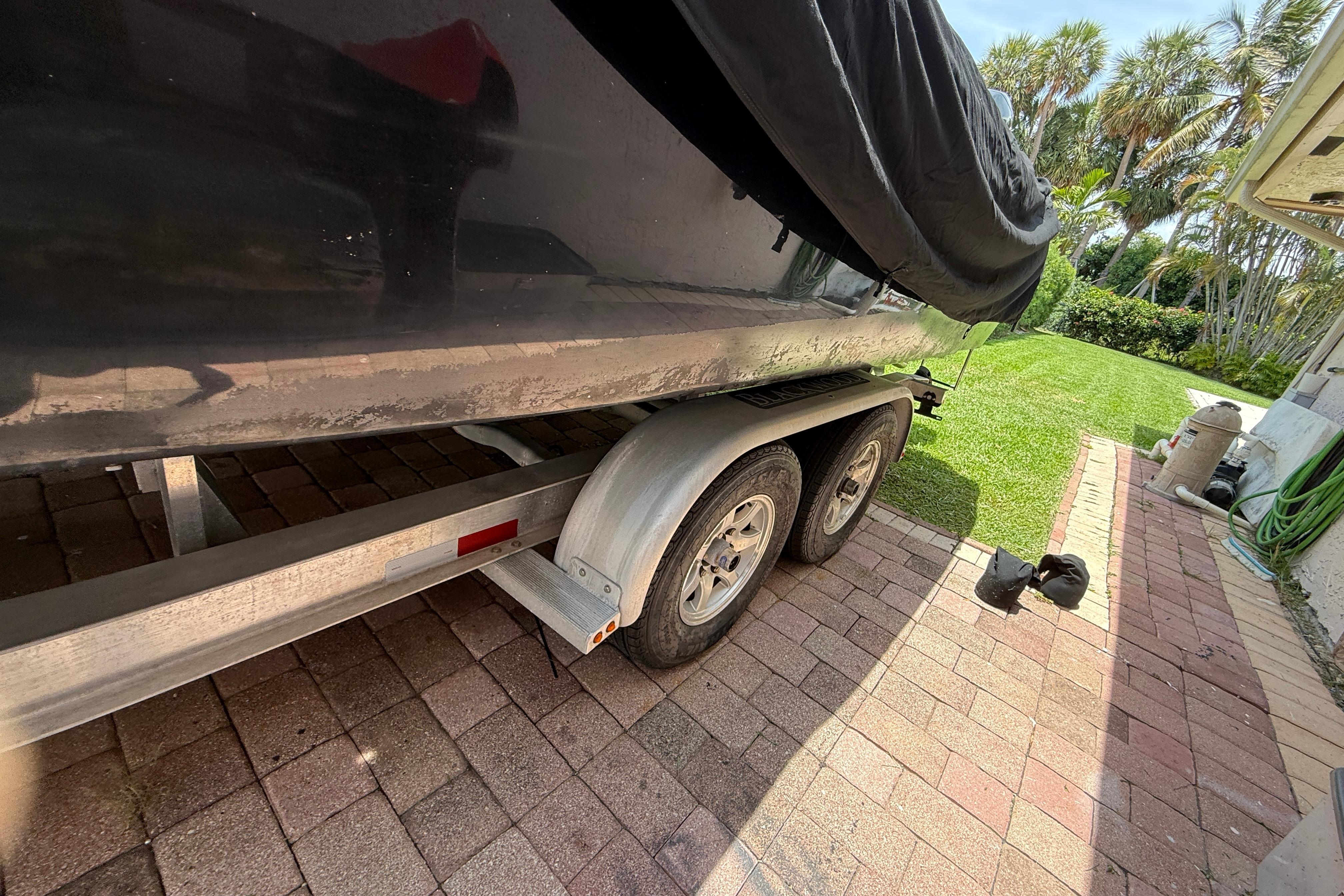 Trailer with a covered 2015 Blackwood 27 boat parked on a brick driveway.