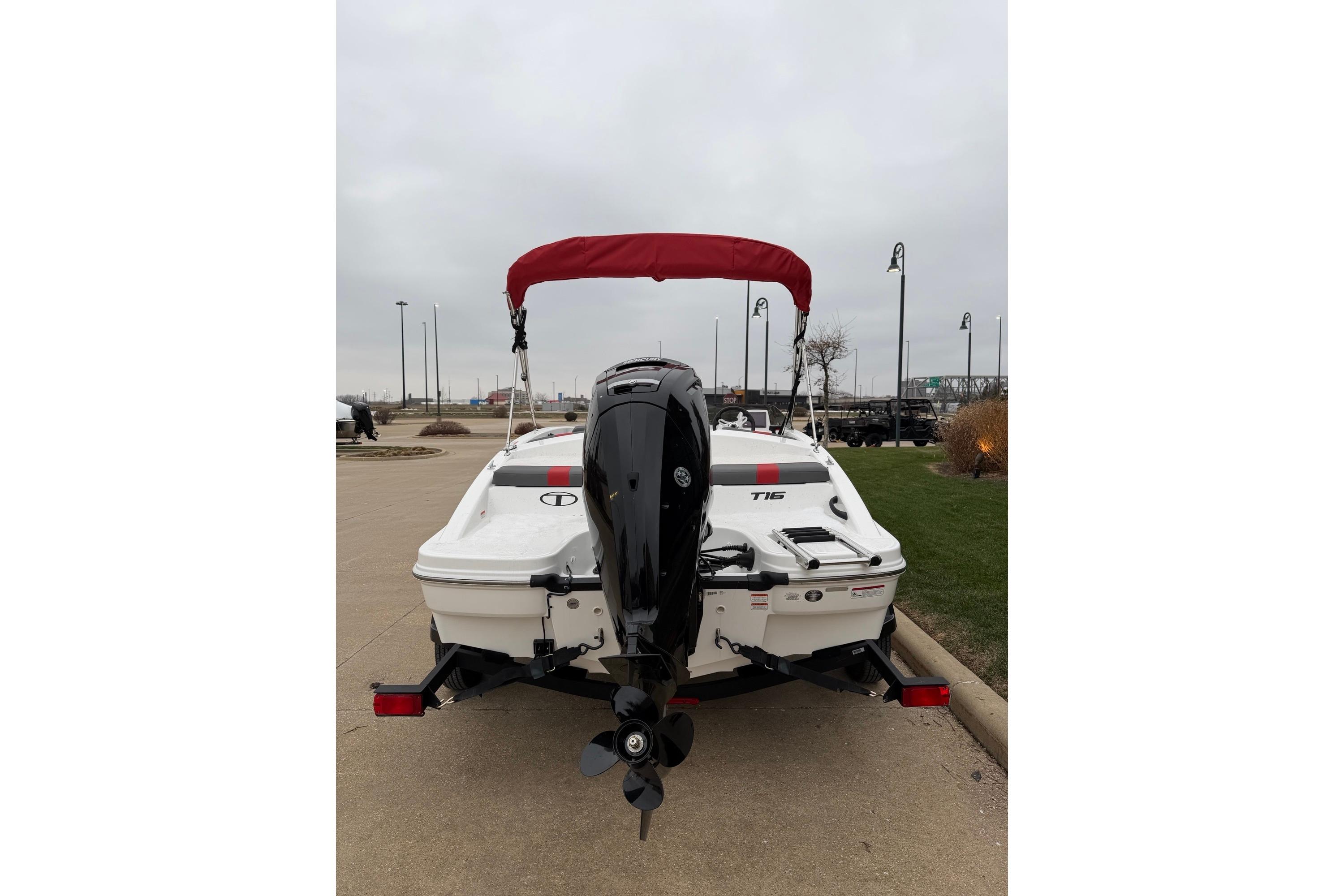 2025 Tahoe T16 boat with red canopy and outboard motor, parked on pavement.