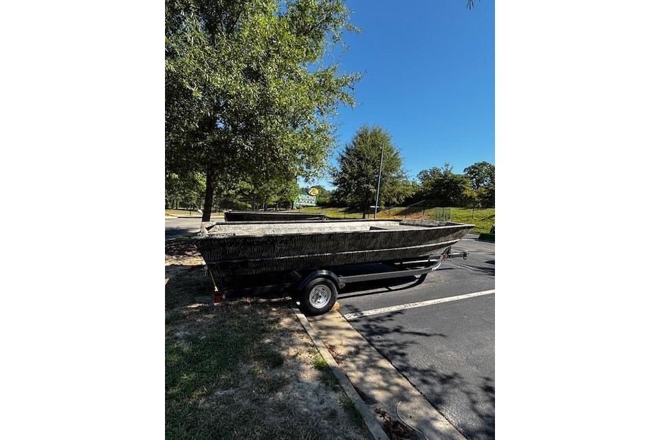 2026 Tracker Grizzly 2072 Utility boat on trailer in parking lot, surrounded by trees.