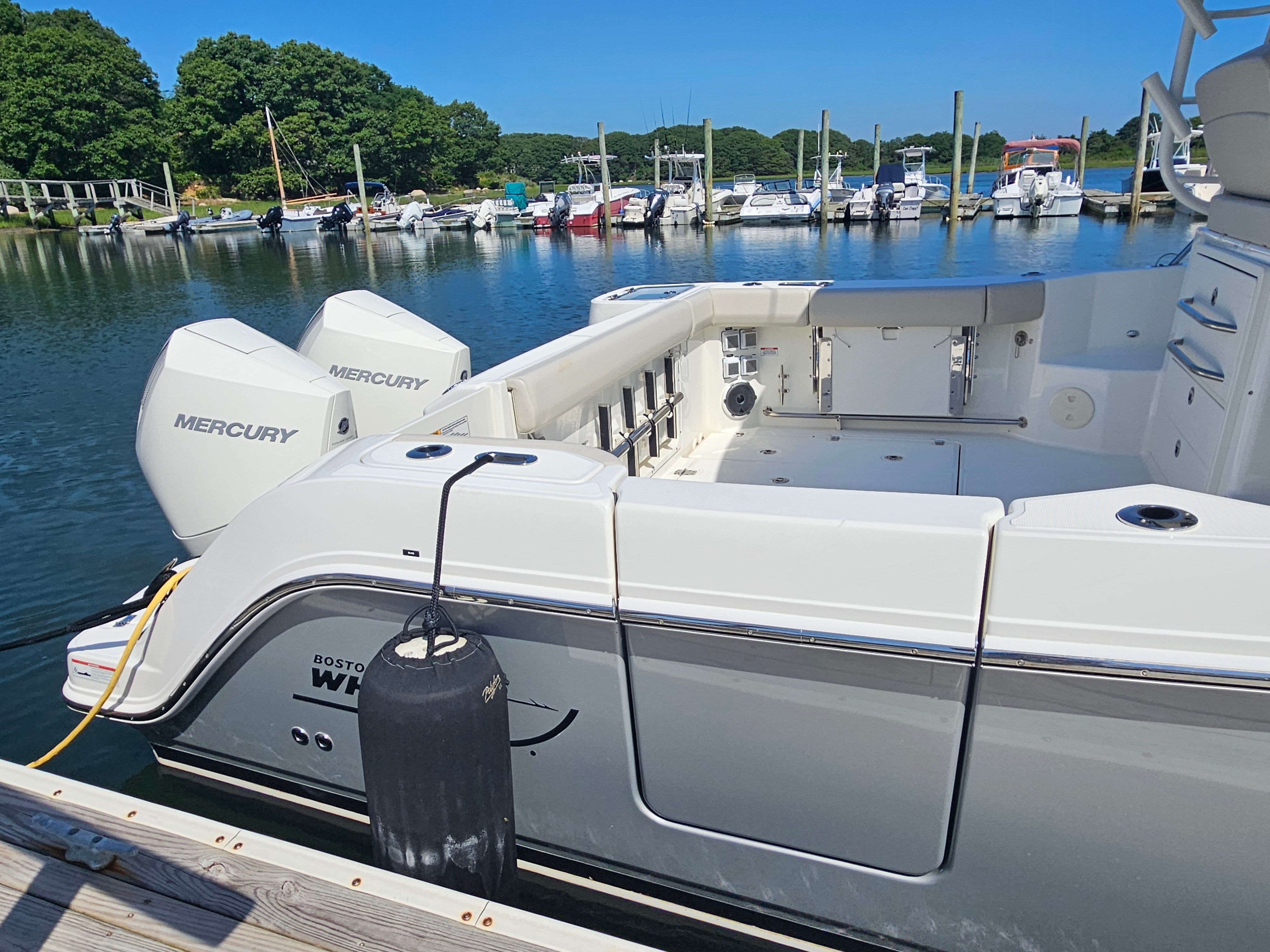 A 2023 Boston Whaler 325 Conquest docked in a calm harbor with other boats.