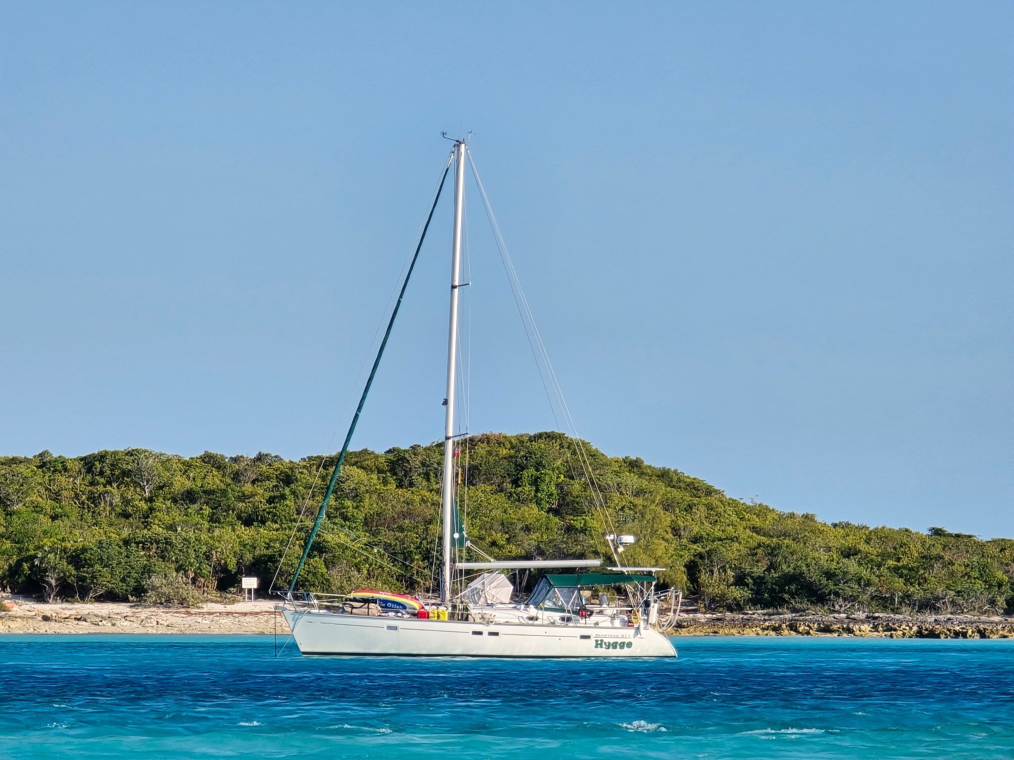 A 1998 Beneteau 411 sails on clear blue water near a wooded coastline.