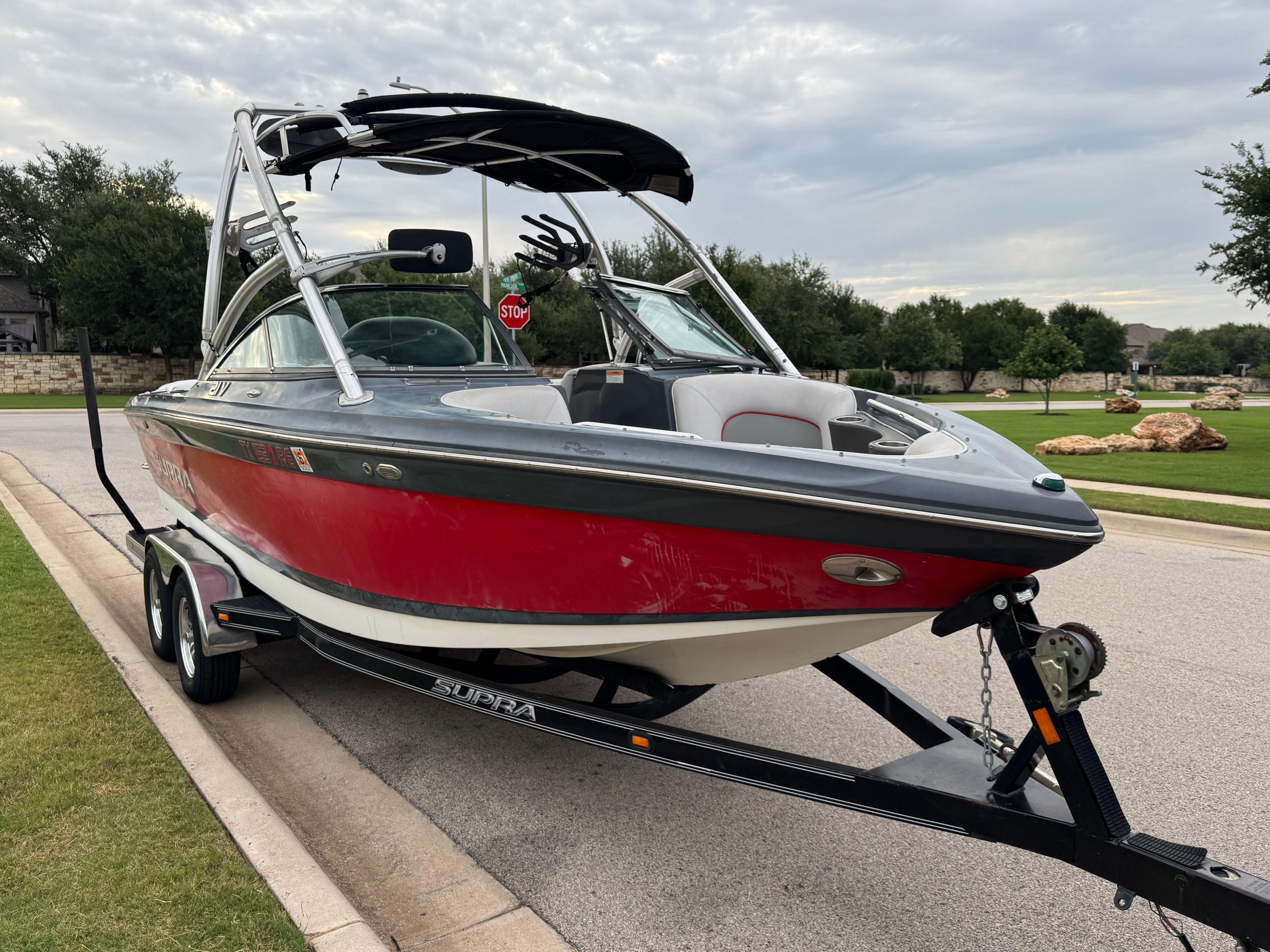 A red 2008 Supra Launch 21 V boat on a trailer, parked on a street.