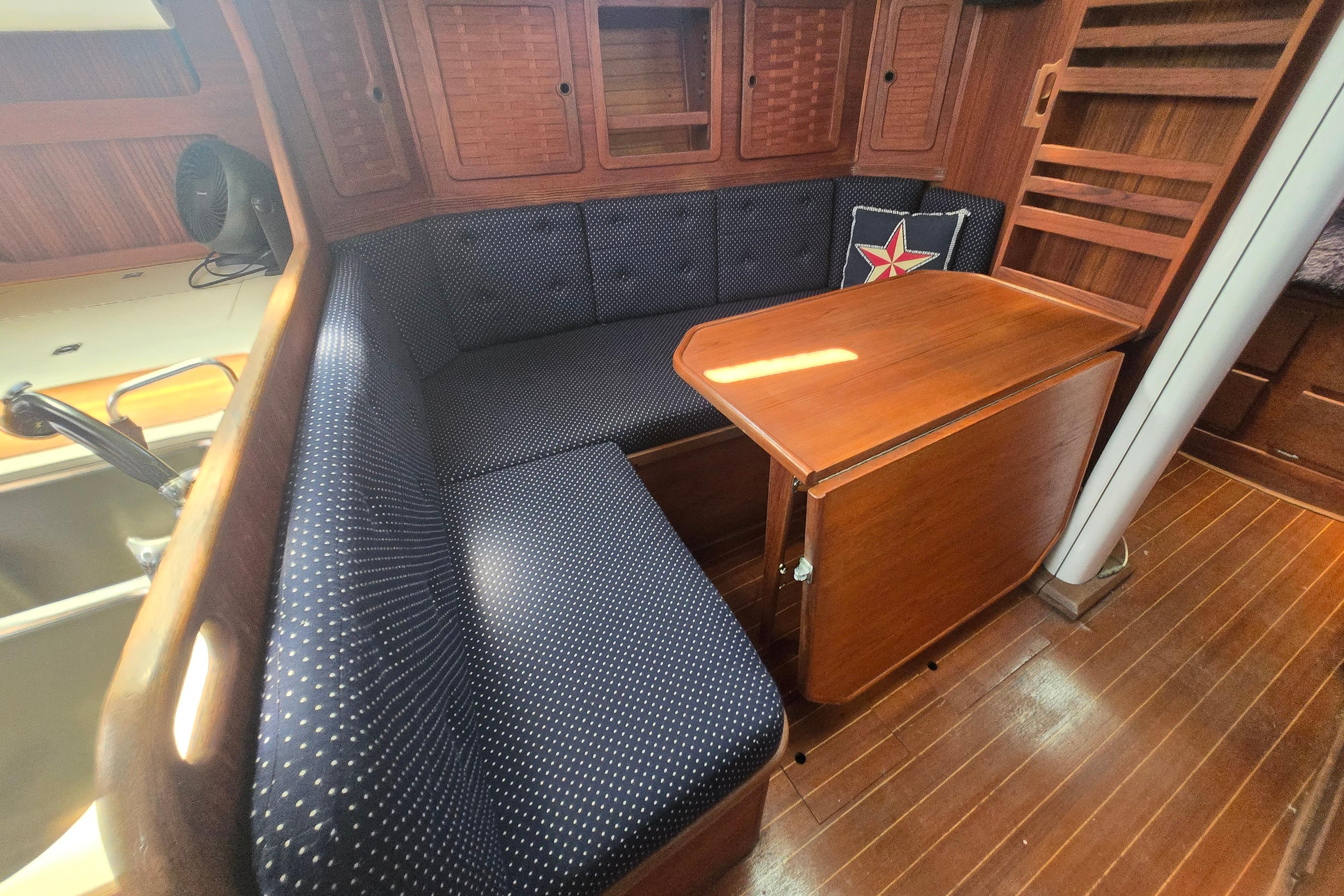 1988 Sabre 38 yacht interior with wooden table, blue cushioned seating, and nautical decor.