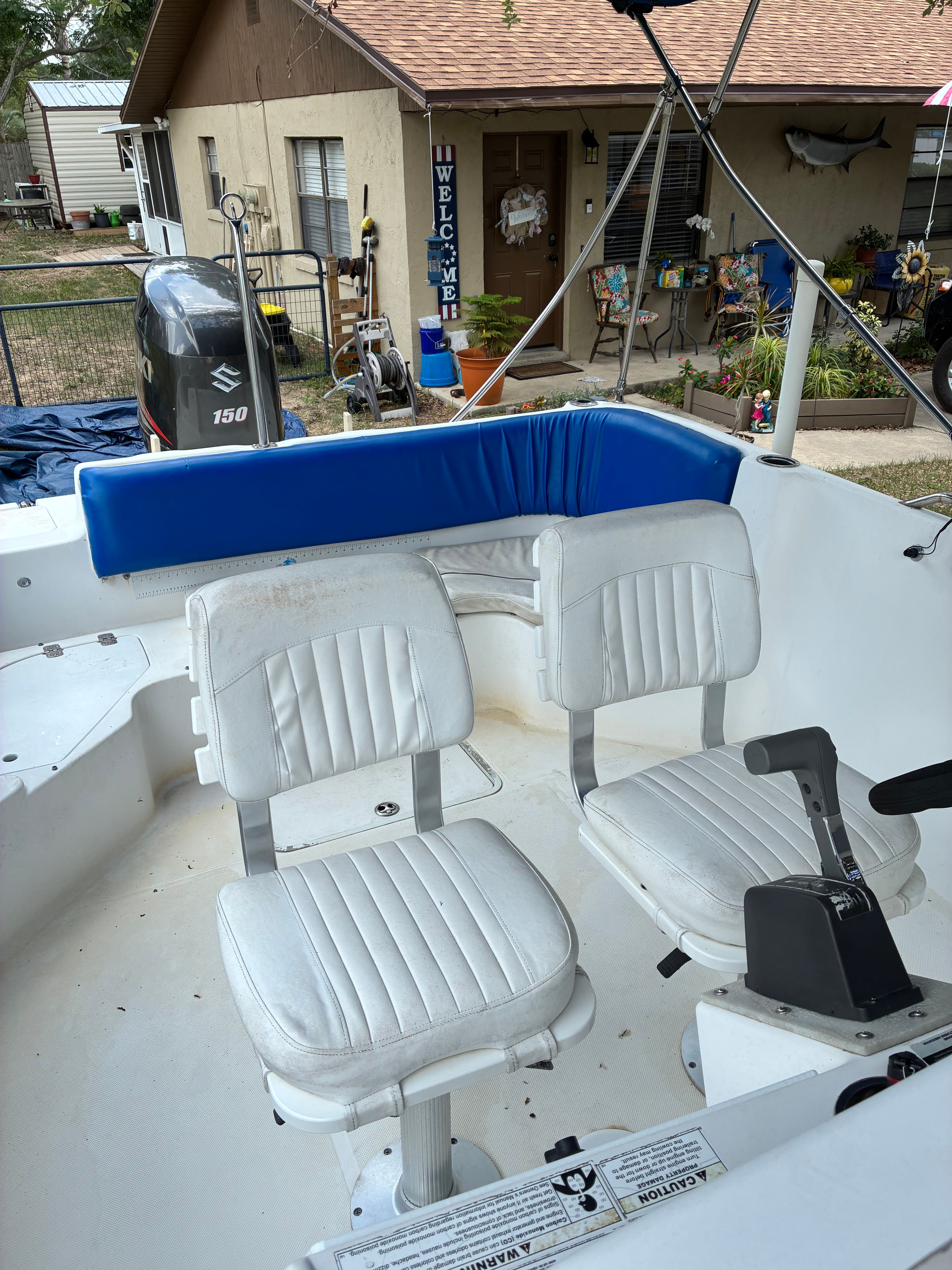 Two white seats in a boat's cockpit with blue padding on the railing.