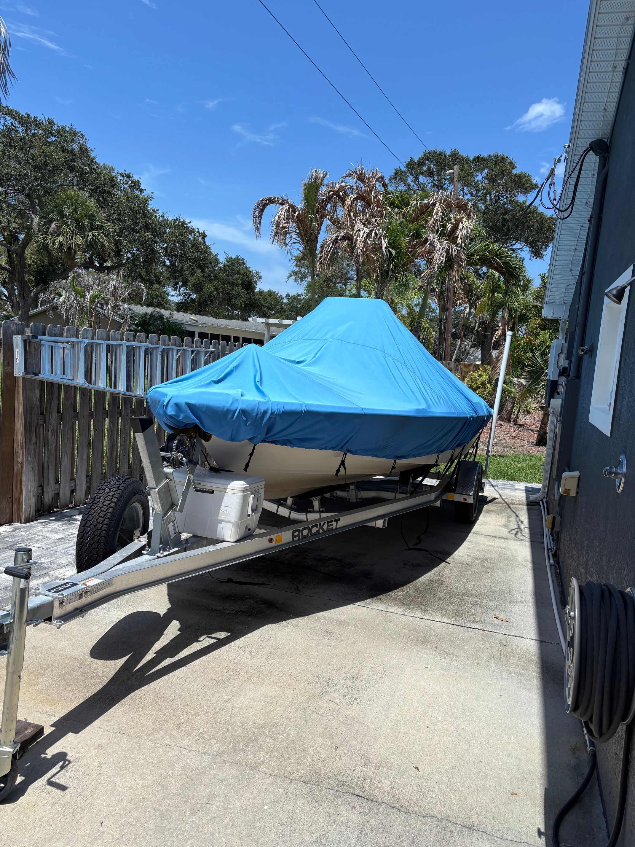 A 2003 Pathfinder 1900T boat on a trailer, covered with a blue tarp, parked in a driveway.