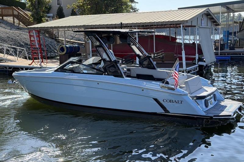2026 Cobalt R8 Surf boat docked on calm water, featuring sleek design and American flag.