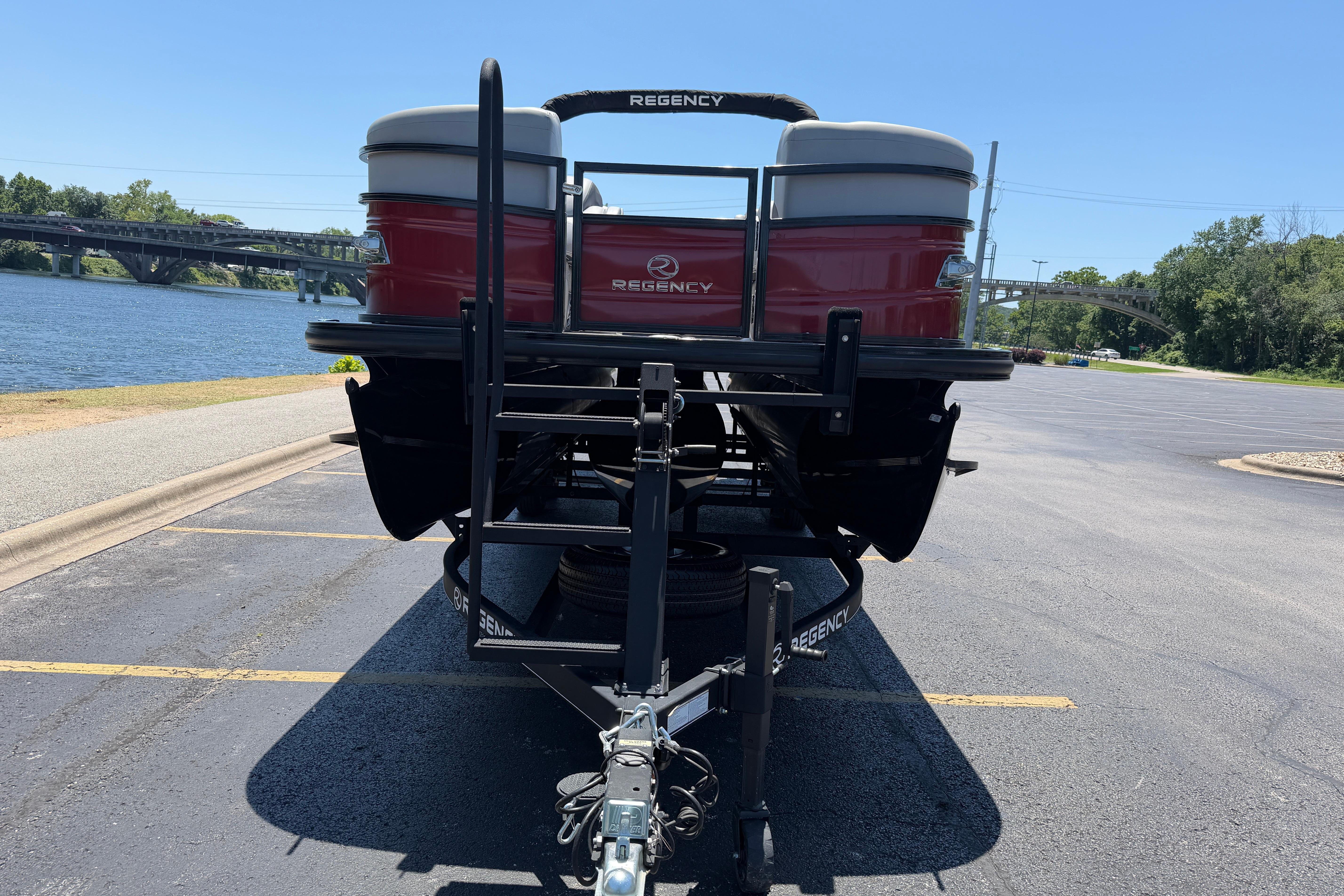 2024 Regency R250DL3 pontoon boat on trailer by a riverside parking lot.
