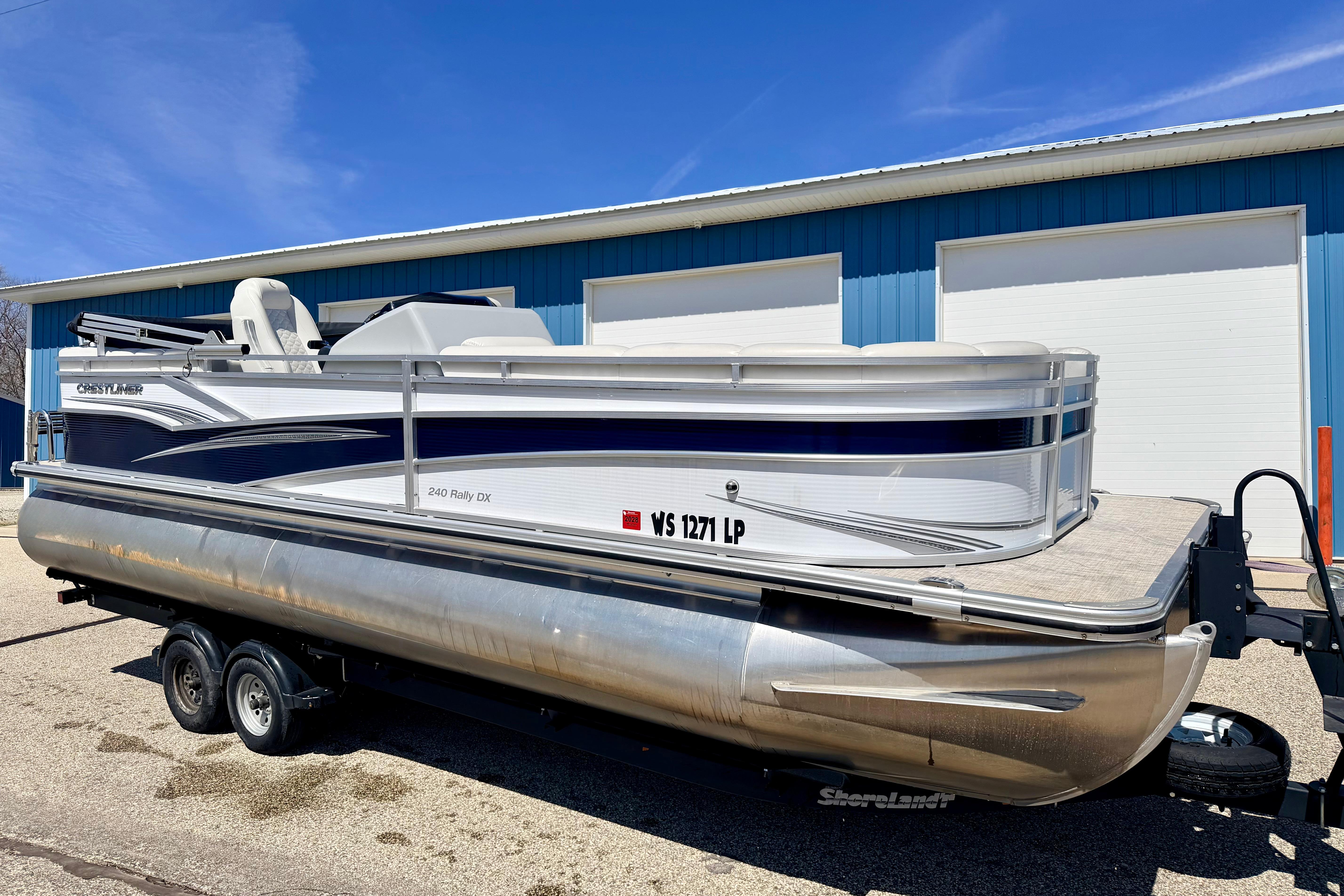 2019 Crestliner 240 Rally DX CW pontoon boat on trailer, parked near blue building.