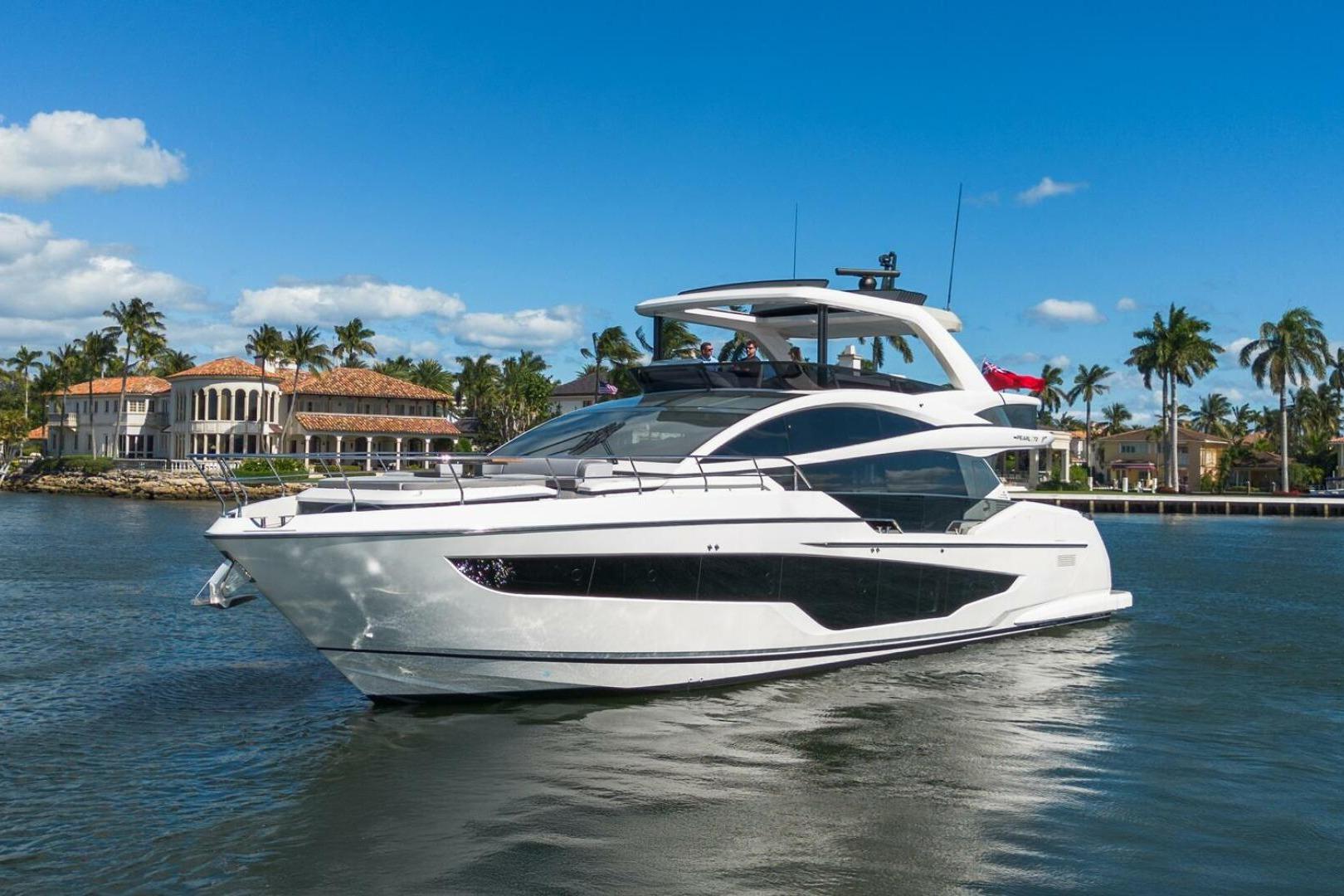Luxurious 2023 Pearl 72 yacht cruising near waterfront mansions and palm trees under a clear blue sky.