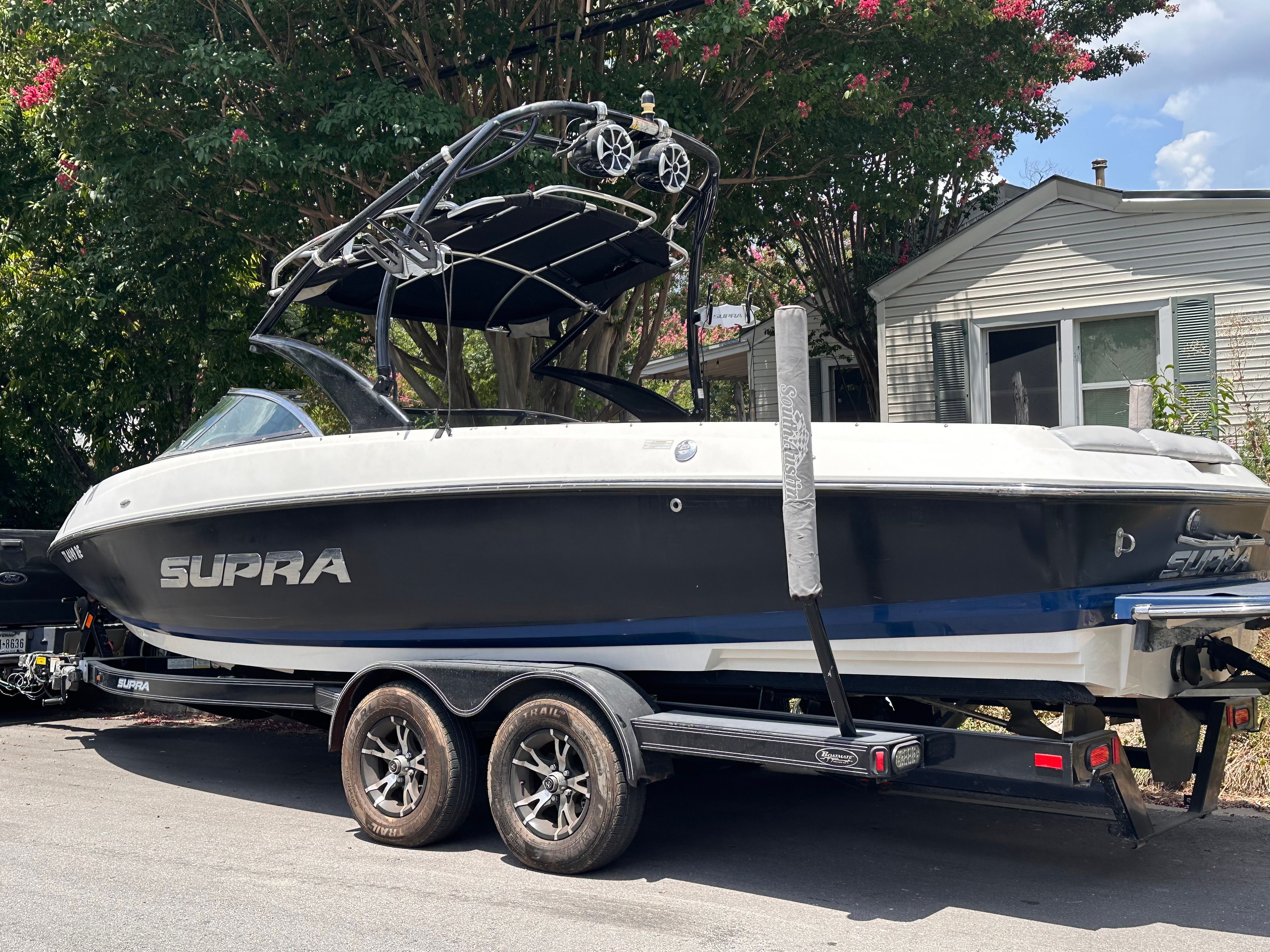 A 2012 Supra Launch 242 boat on a trailer parked in front of a house.