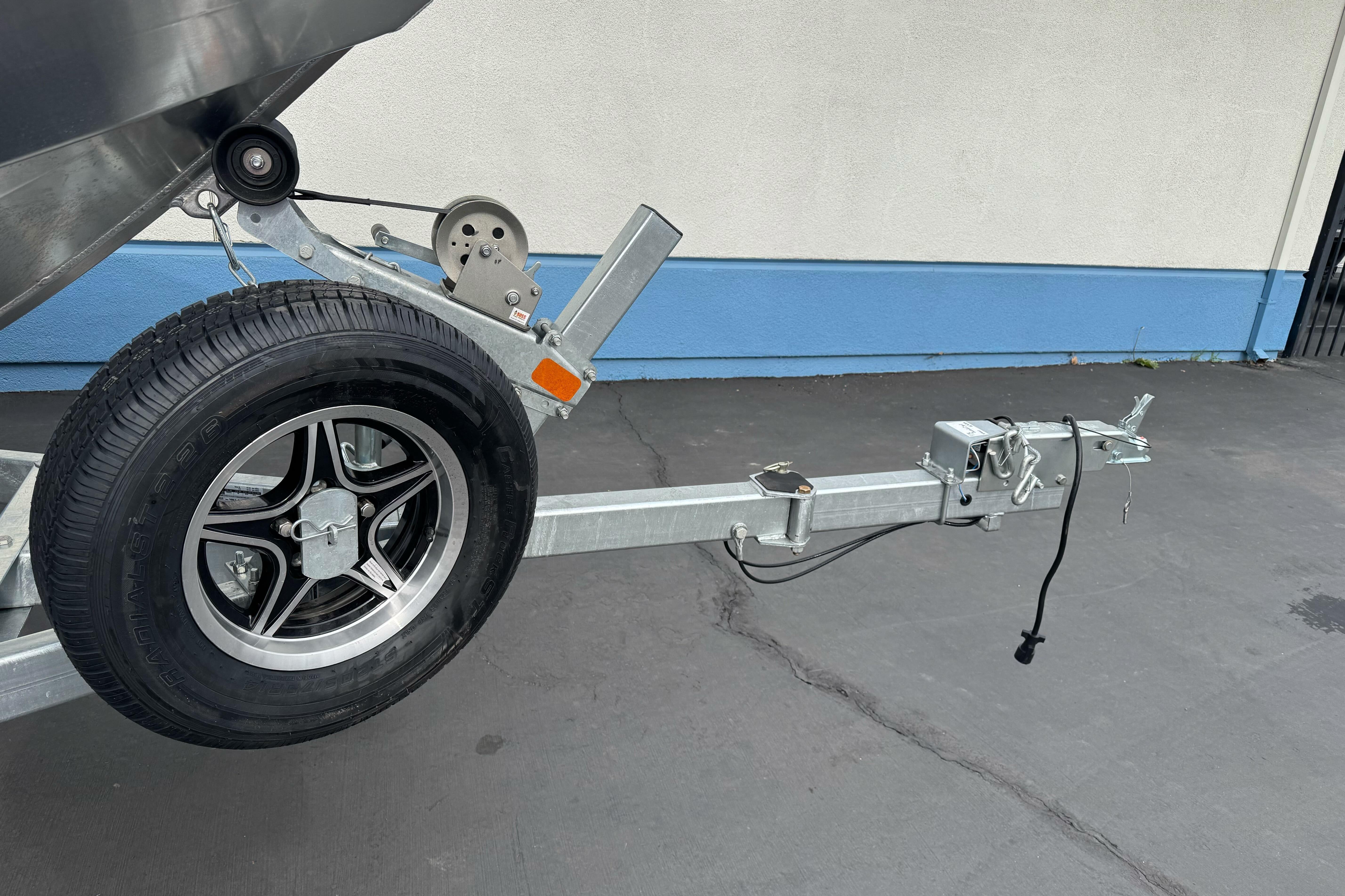 Trailer hitch and wheel of 2026 Lund 185 Heavy Gauge boat on pavement.