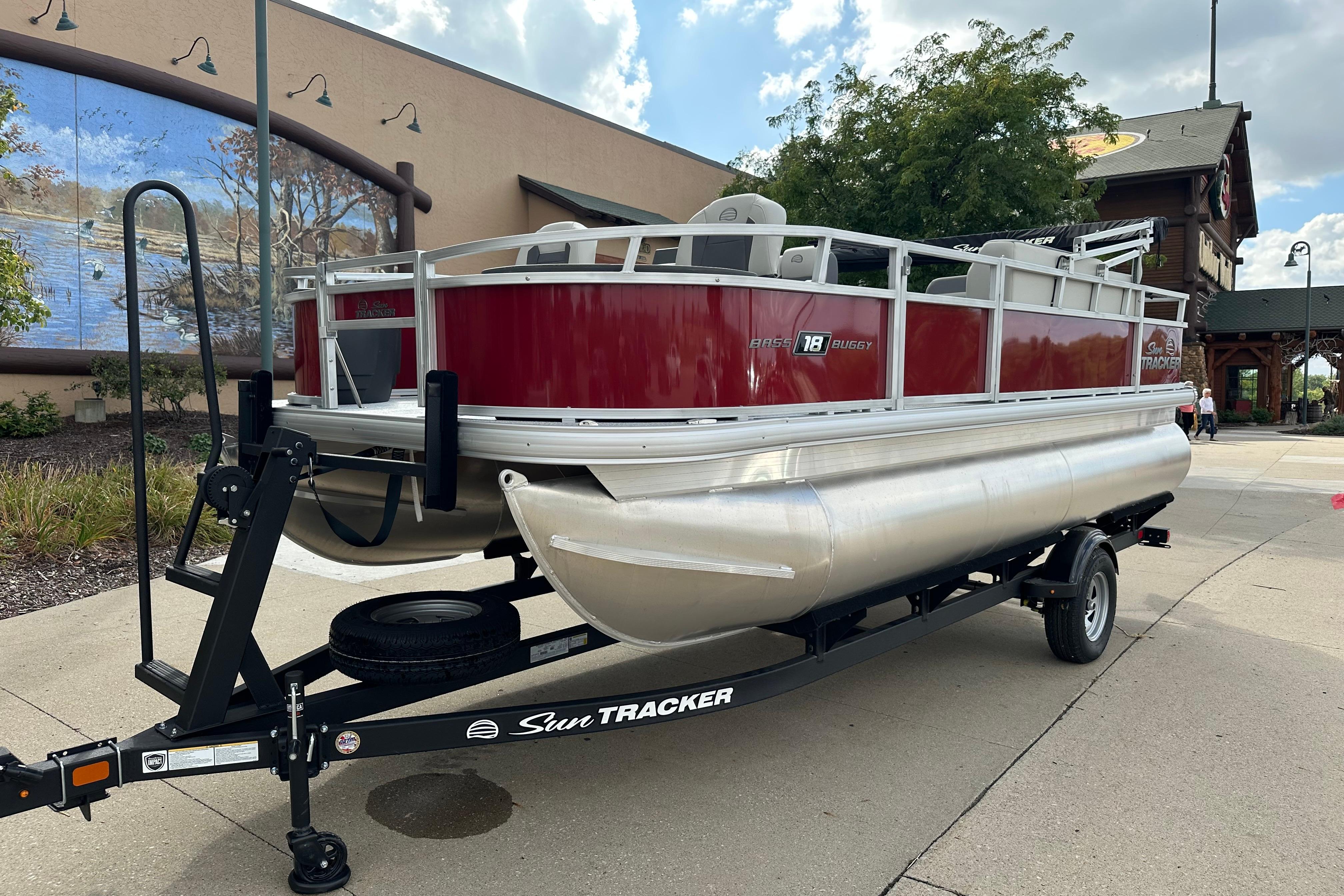 2026 Sun Tracker Bass Buggy 18 DLX pontoon boat on trailer, parked outdoors.