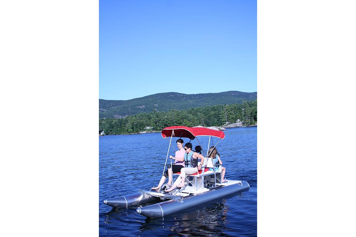 People enjoying a ride on a 2026 Aqua Cycle 2 pedal boat with a red canopy.
