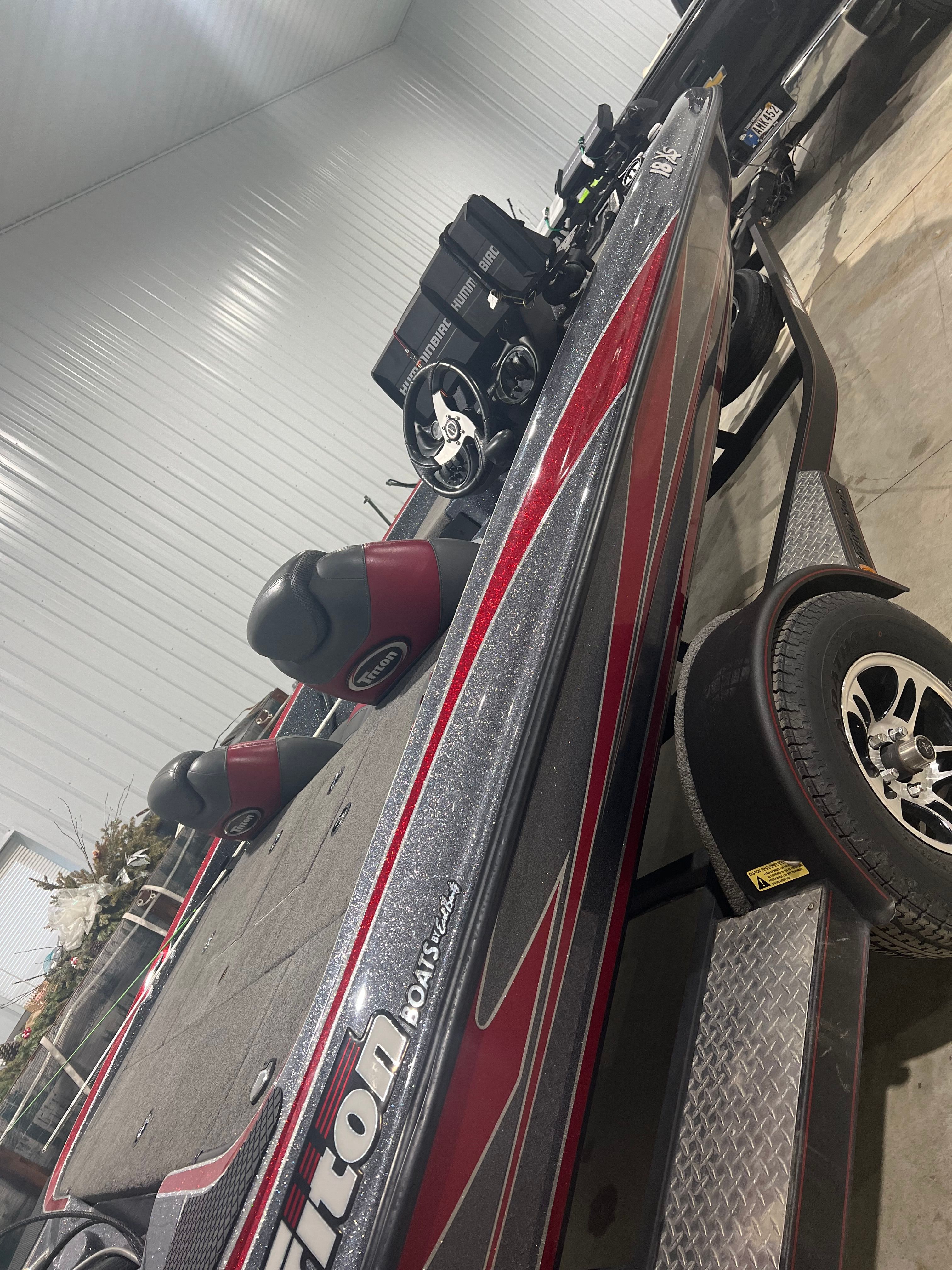 A 2015 Triton 18XS boat in a warehouse, featuring a red and black design and a trailer.