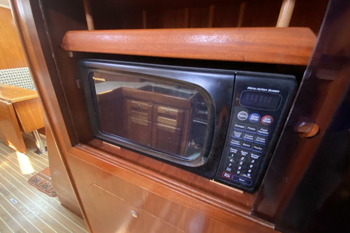 Microwave in 1999 Dufour 39 CC yacht interior, featuring wooden cabinetry.