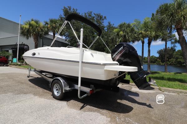 2018 Bayliner 210 DB boat on trailer, parked near palm trees and water.