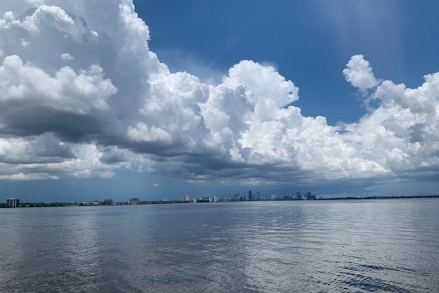 Expansive cloudy sky over calm water with distant city skyline.