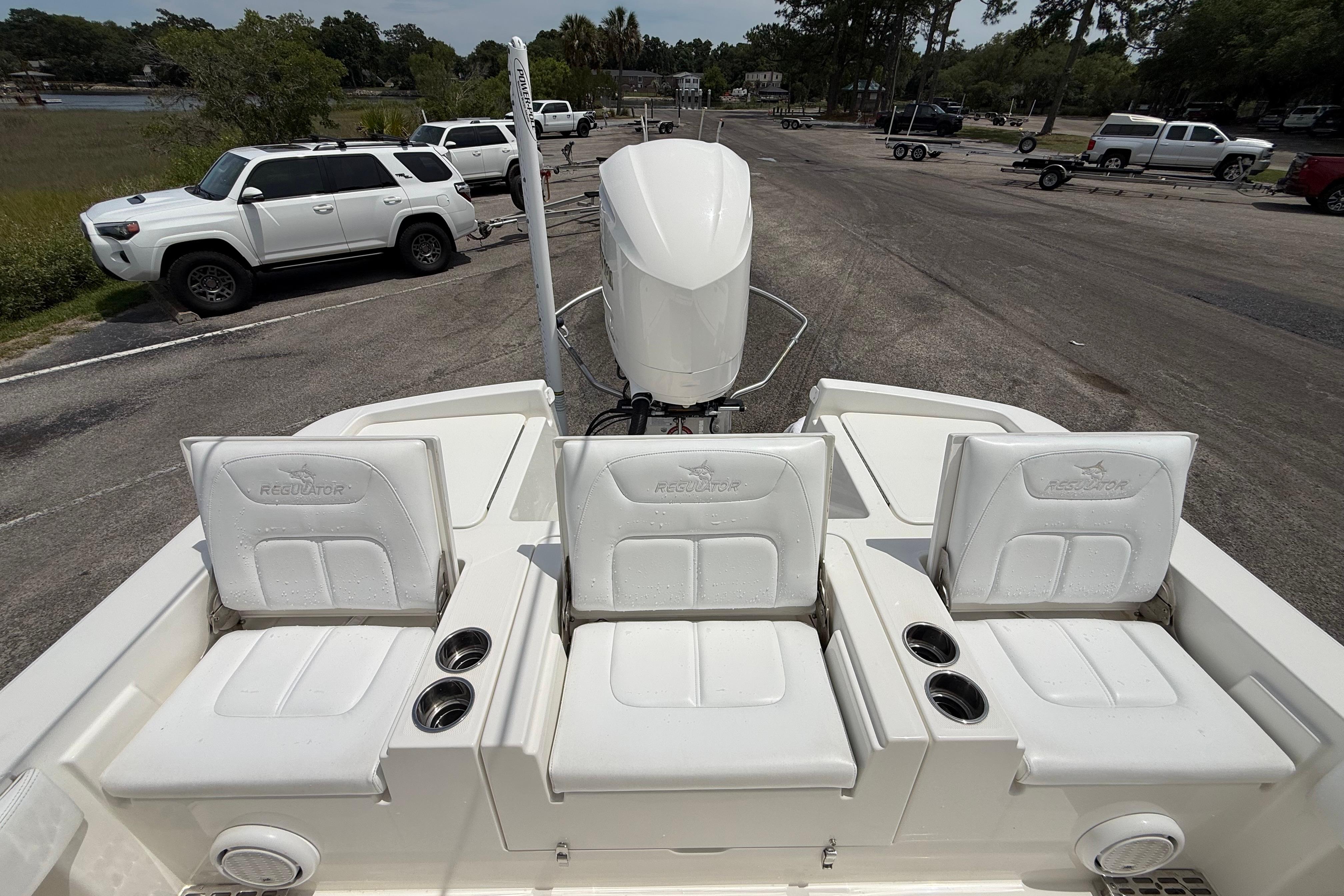 2019 Regulator 26XO boat with white seating and motor, parked near vehicles.