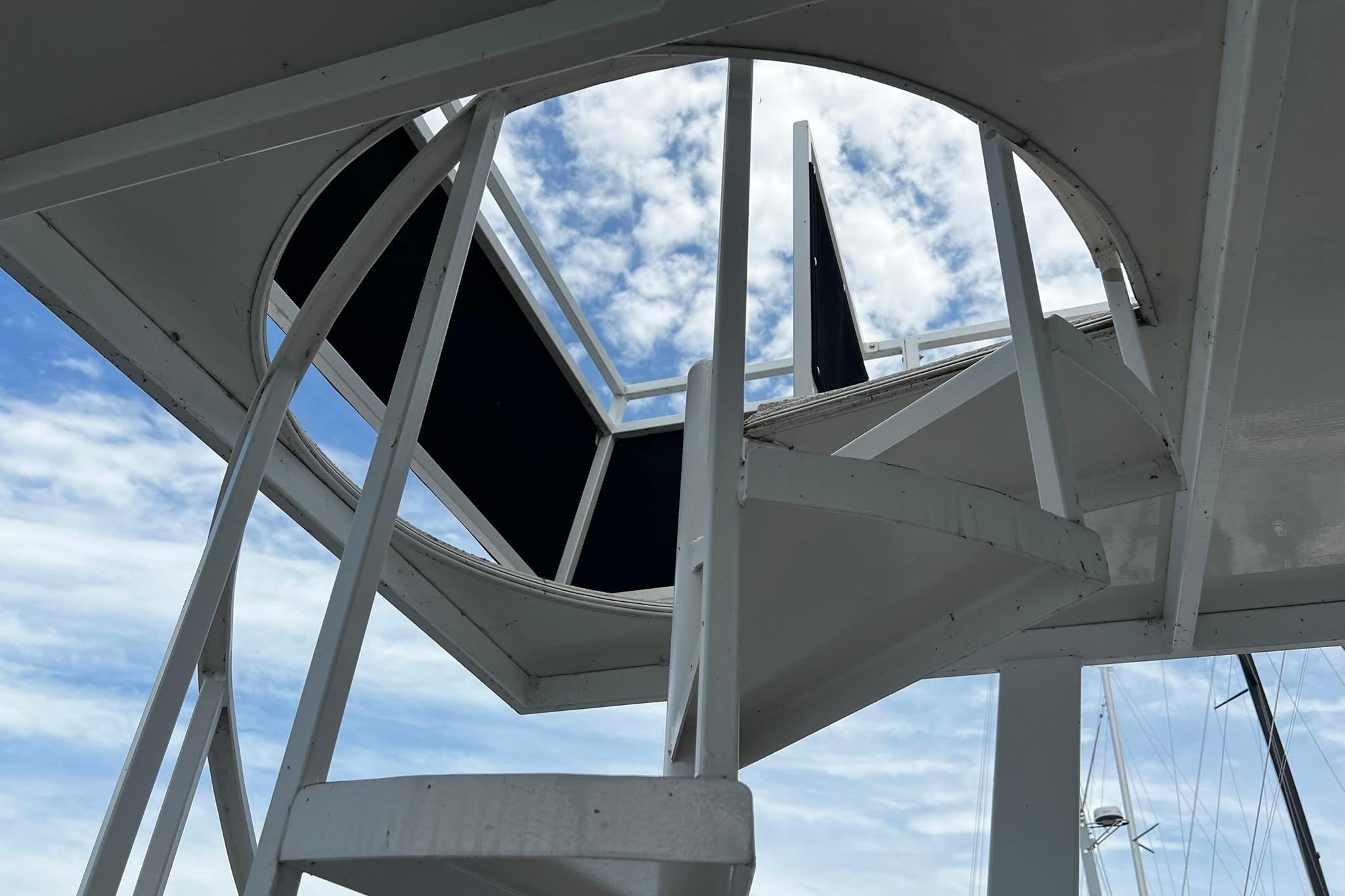 Spiral staircase on 2010 Skipperliner 480 Flybridge against a cloudy sky.
