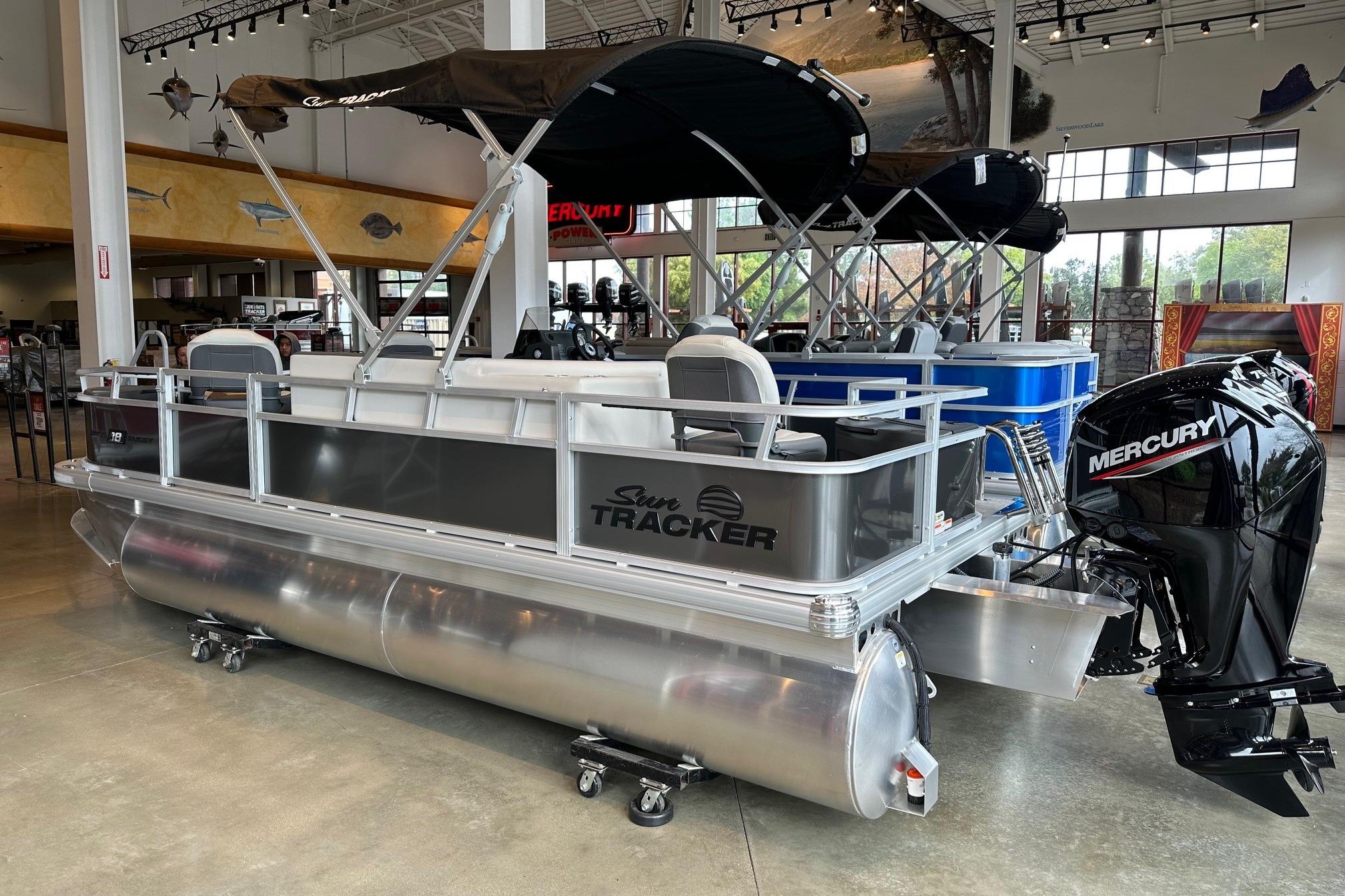 2026 Sun Tracker Bass Buggy 18 DLX pontoon boat with Mercury engine in showroom.