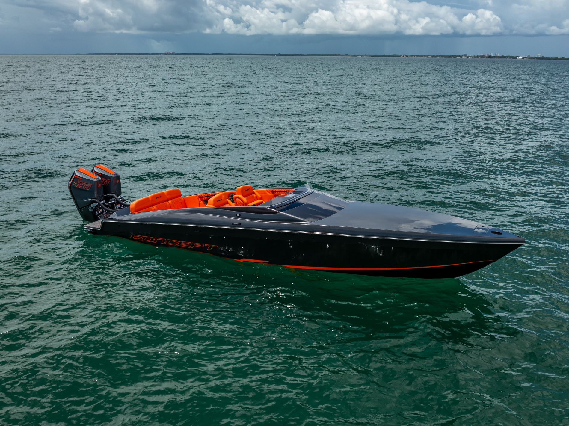 A black sport boat with orange accents floats on calm water under a cloudy sky.
