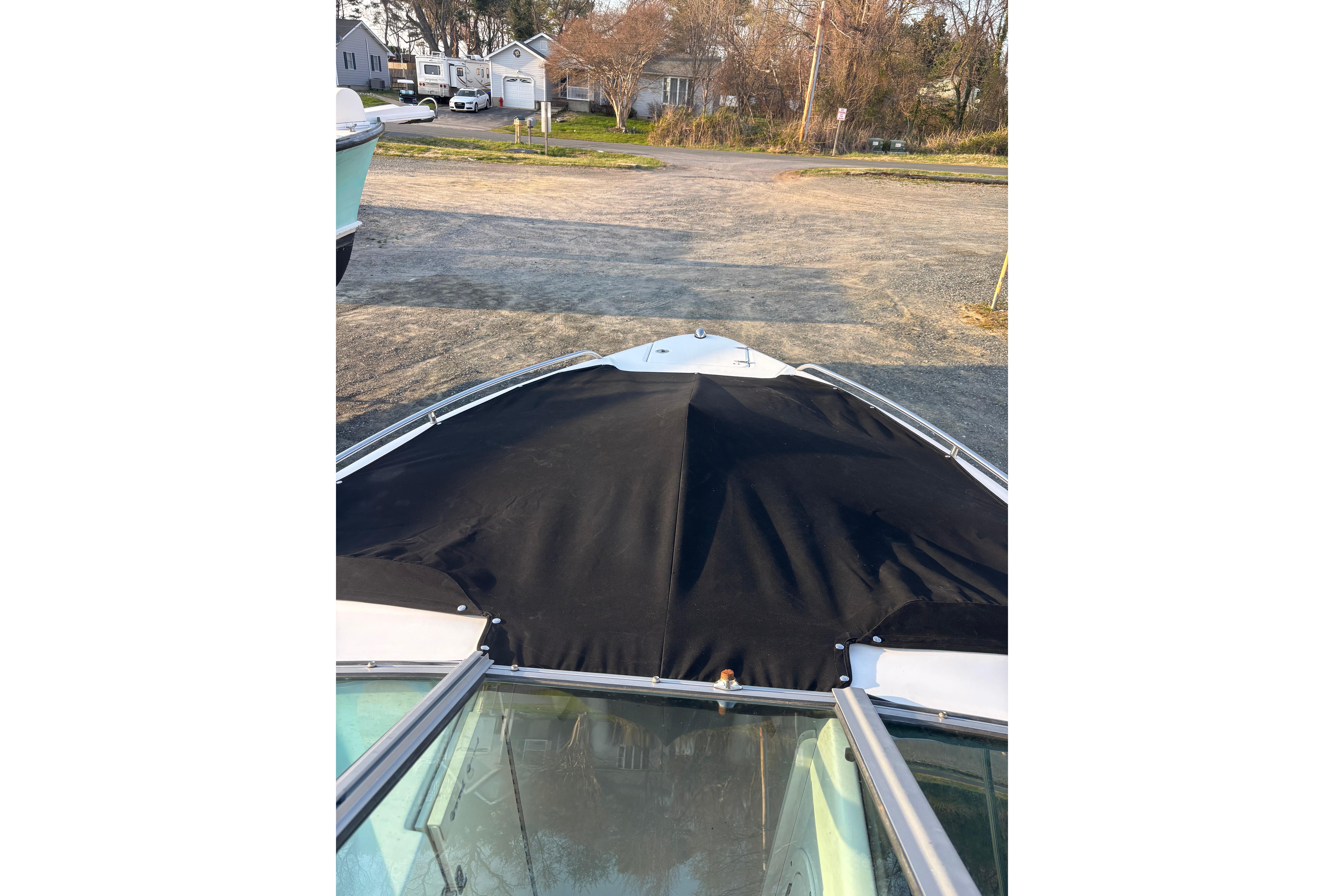 2012 Chaparral 267 SSX boat with black cover, parked on a gravel lot.