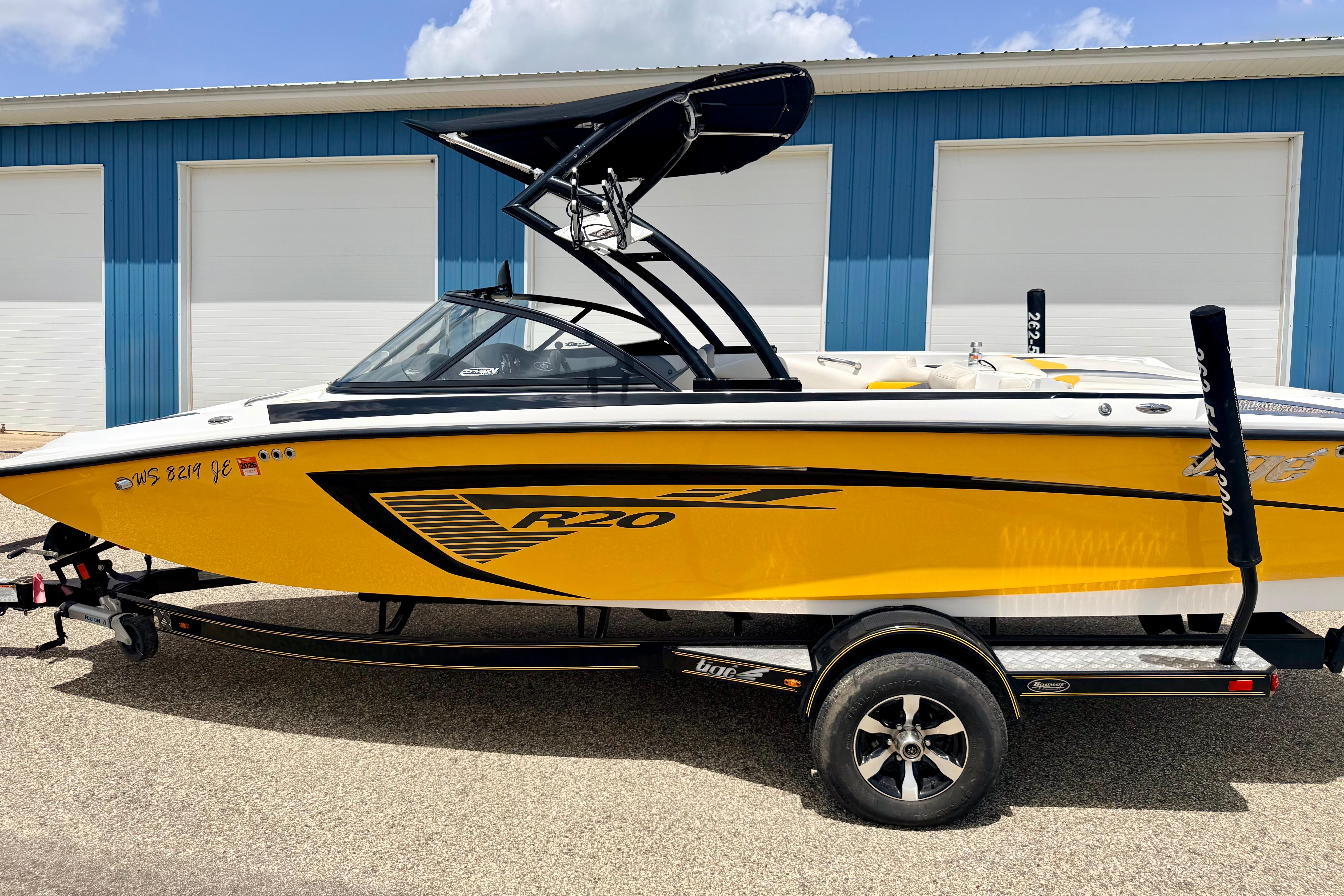 2014 Tigé R20 boat in vibrant yellow, parked on a trailer near blue garage doors.