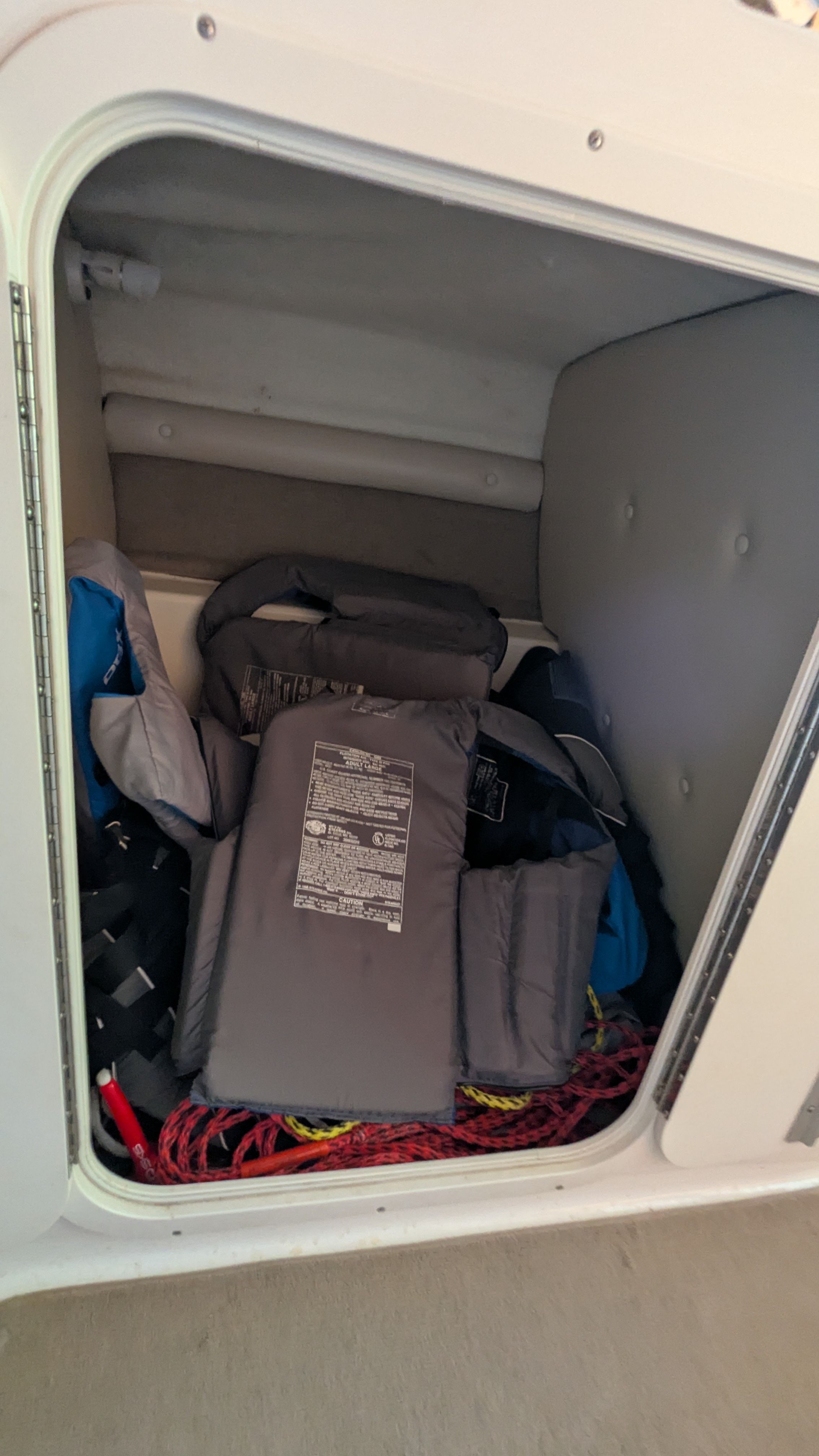 A storage compartment in the boat with several life jackets and ropes.