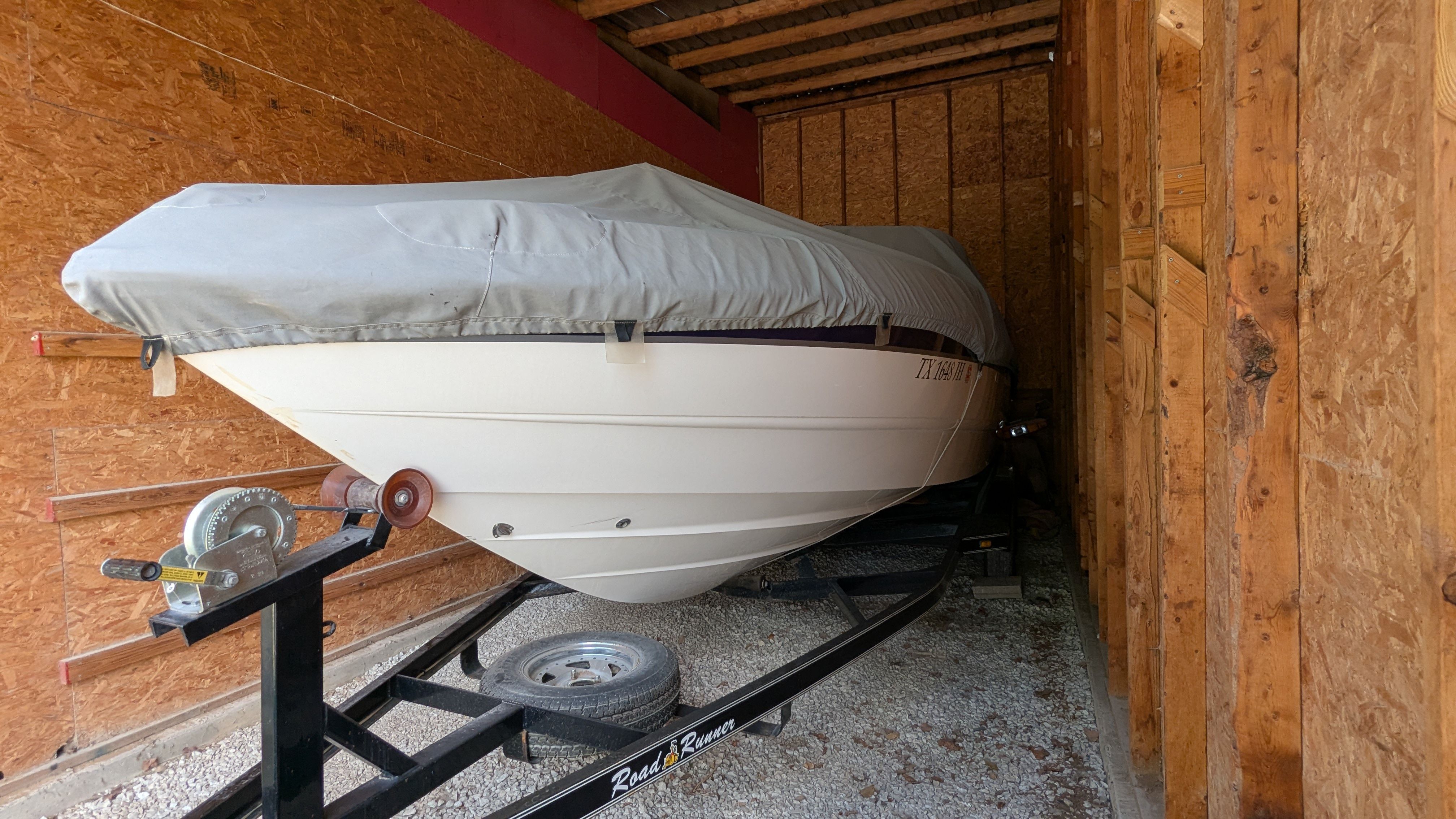 A 2000 Chaparral 240 SSi boat, covered and stored on a trailer in a wooden shed.