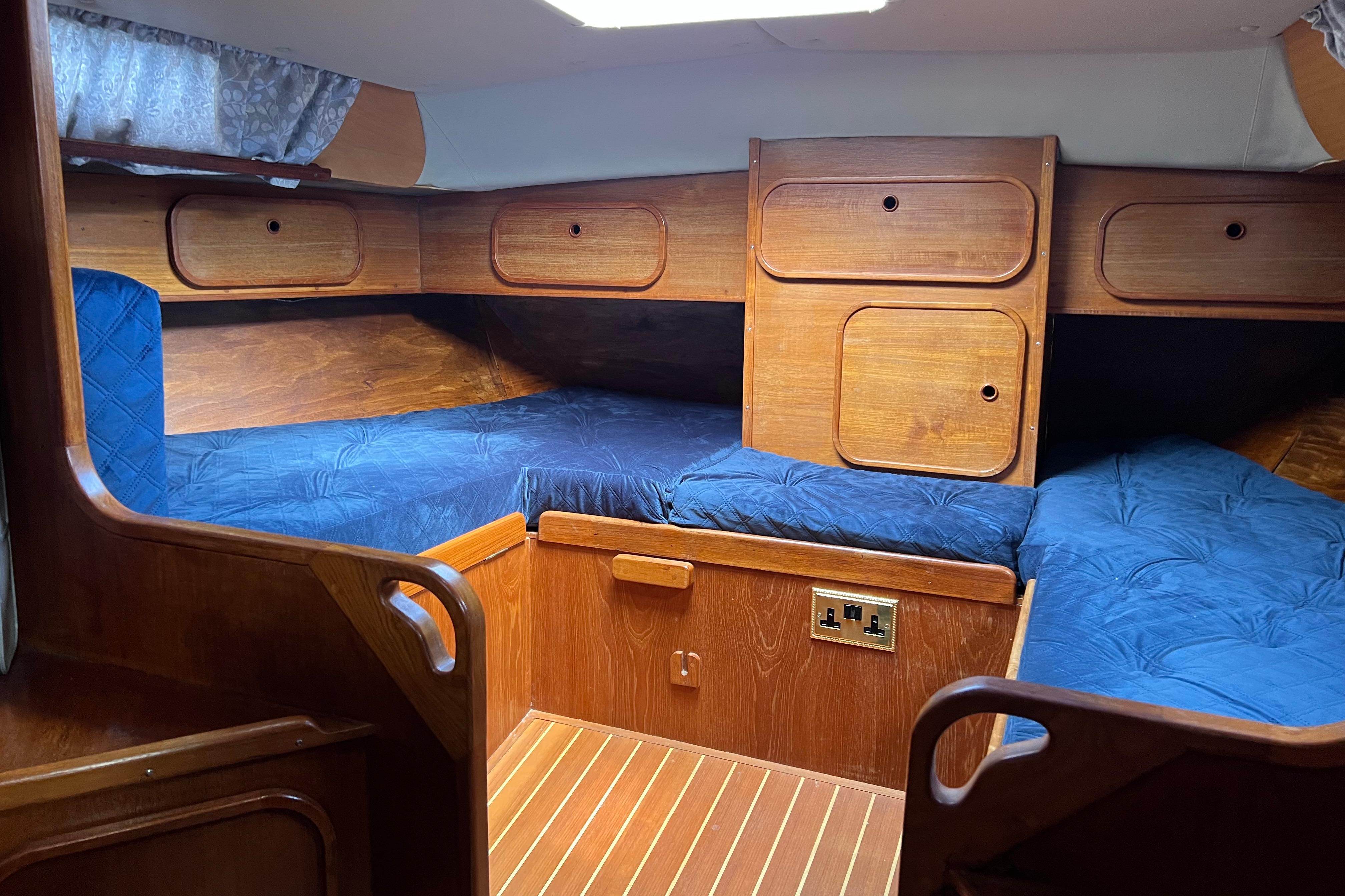 Cozy cabin interior of 1983 Westerly Sealord 39 sailboat with blue cushions and wooden finish.