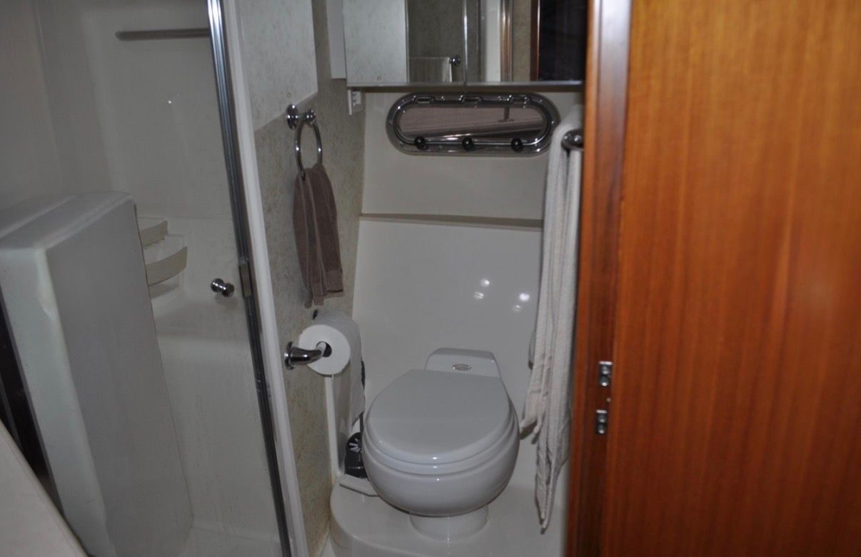 The image shows a yacht bathroom with a toilet, shower, and towel rack.