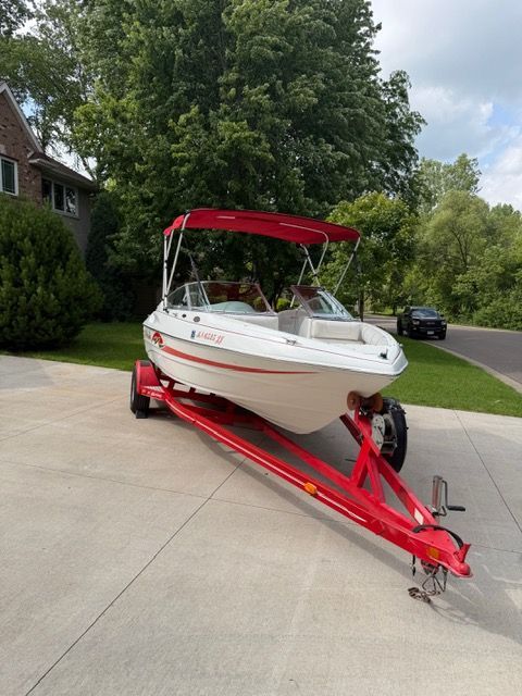 A white boat with a red canopy sits on a trailer in a driveway.