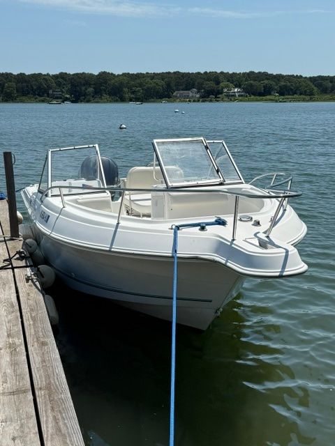 A 1999 Aquasport 215 DC docked at a pier. It's a white boat with an open deck.