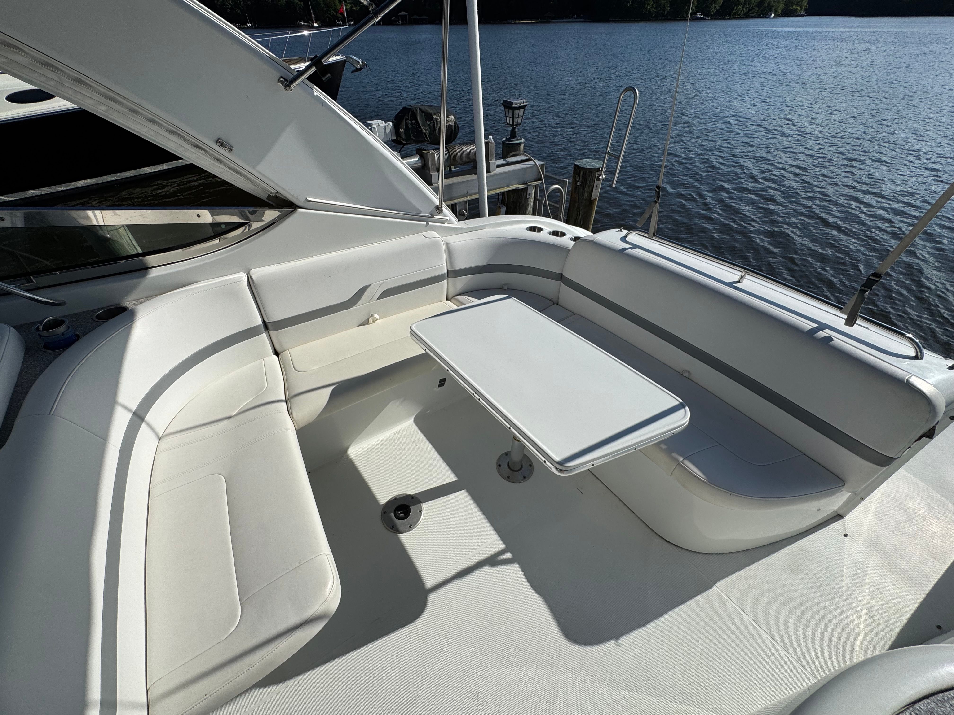 A sleek boat with white seating and a table, docked by the water.